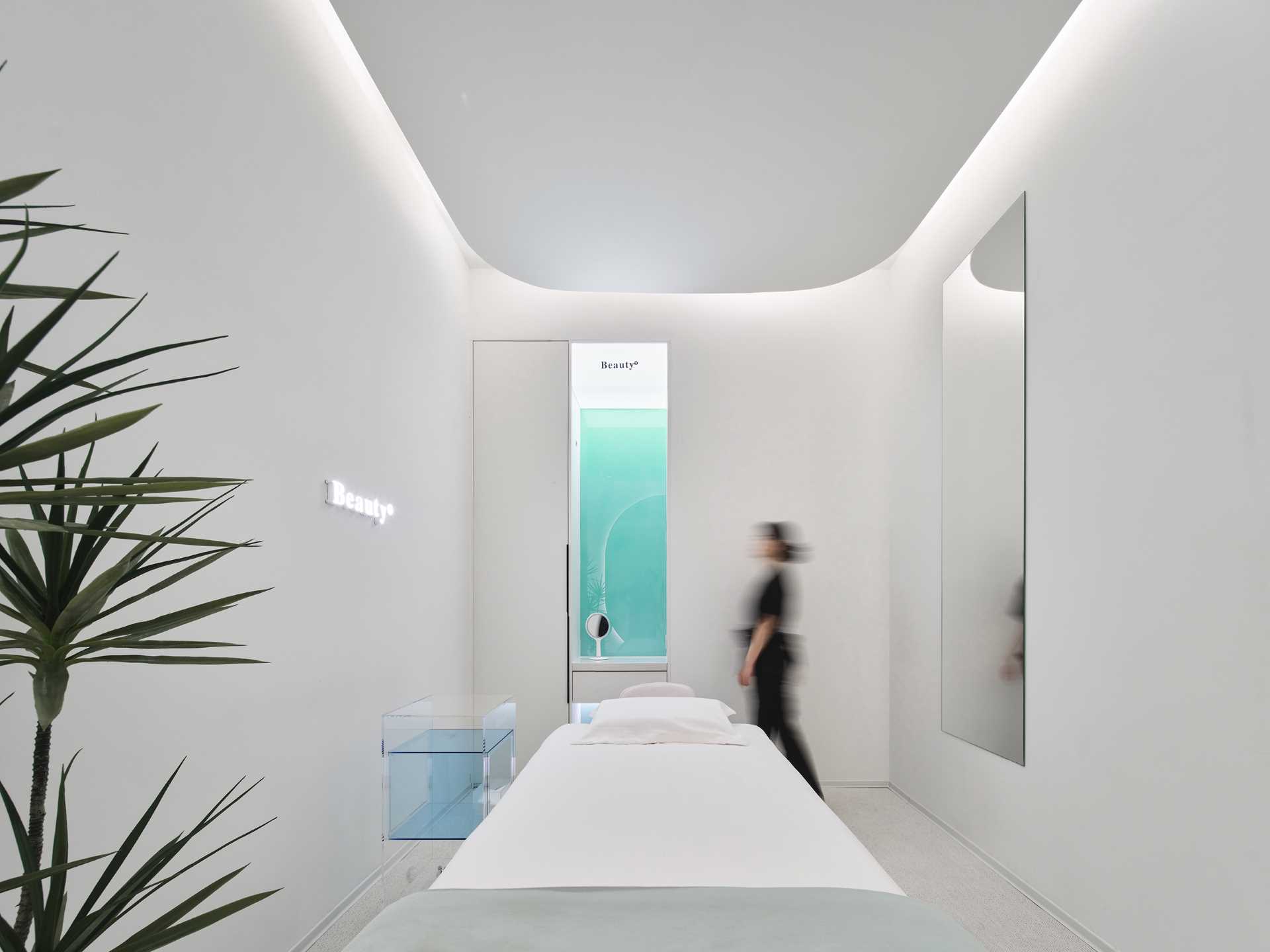 The single-person treatment room has a rectangular layout with a rounded ceiling detail to soften the corners. A large mirror makes the space feel larger, while the opposite wall features a blue-green gradient glass accent.