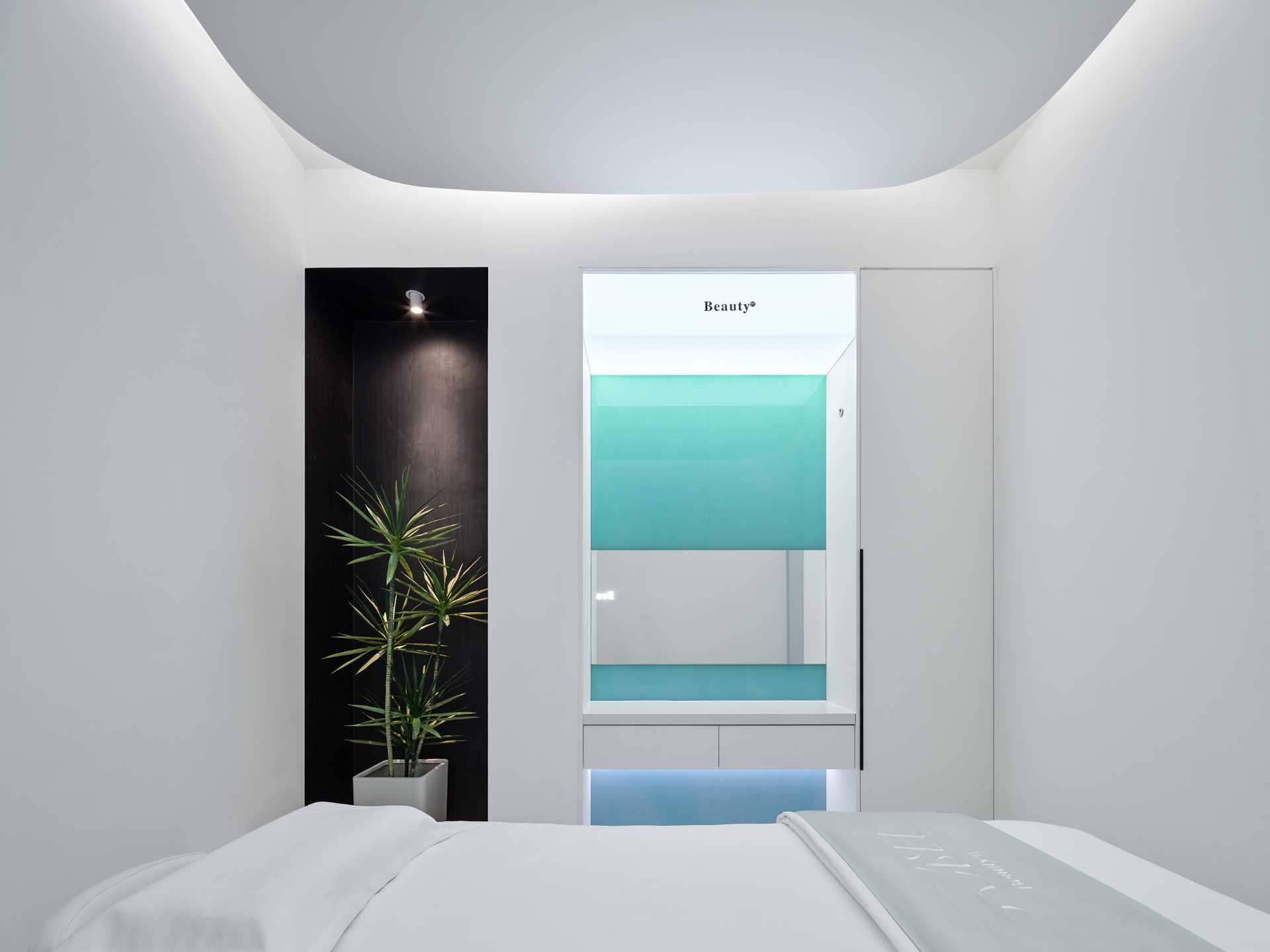 The single-person treatment room has a rectangular layout with a rounded ceiling detail to soften the corners. A large mirror makes the space feel larger, while the opposite wall features a blue-green gradient glass accent.