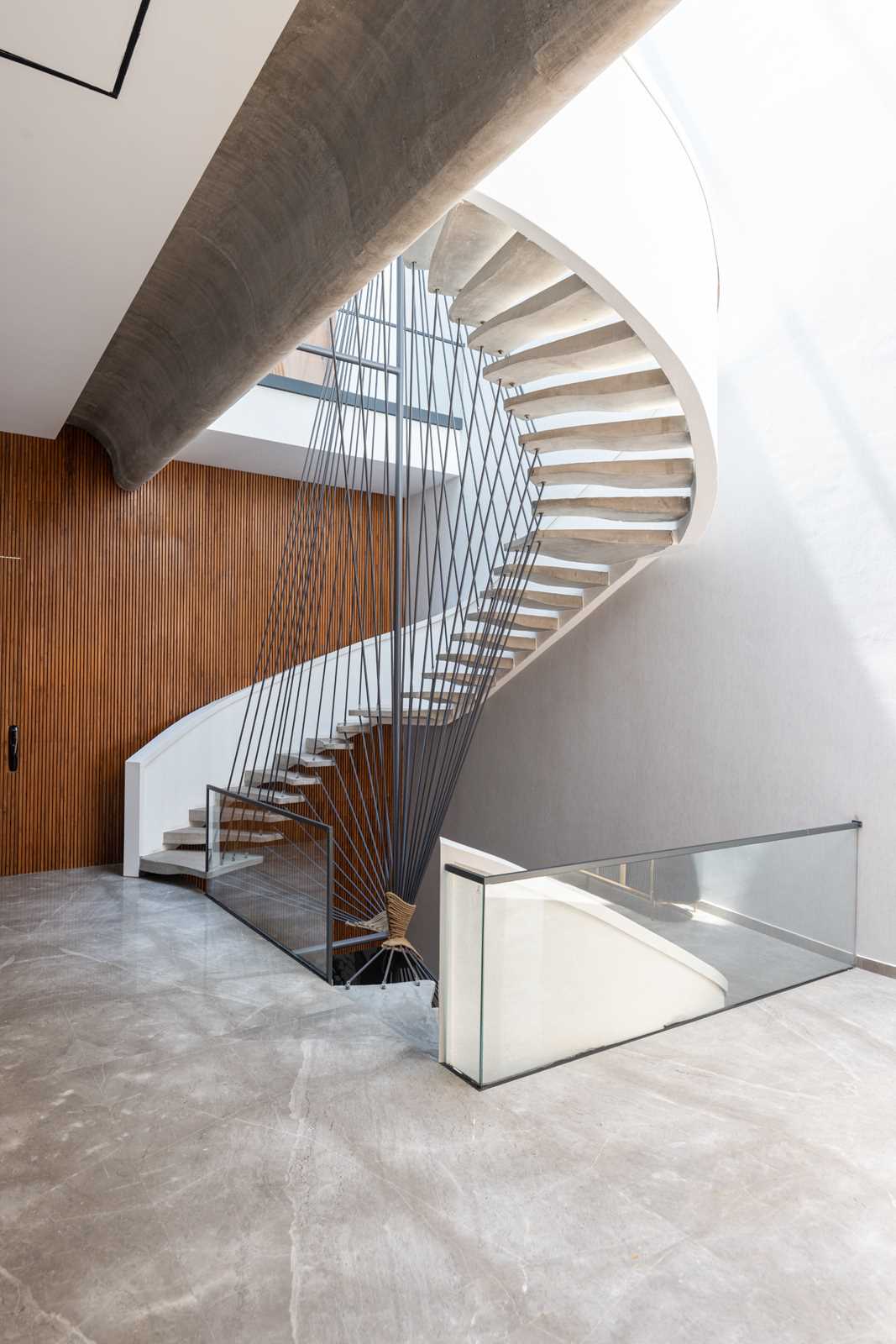 A spiral staircase with an artistic wire detail, giving the illusion of a puzzle, connecting the vertical spaces, and unfurling itself as one ascends to the upper floors.