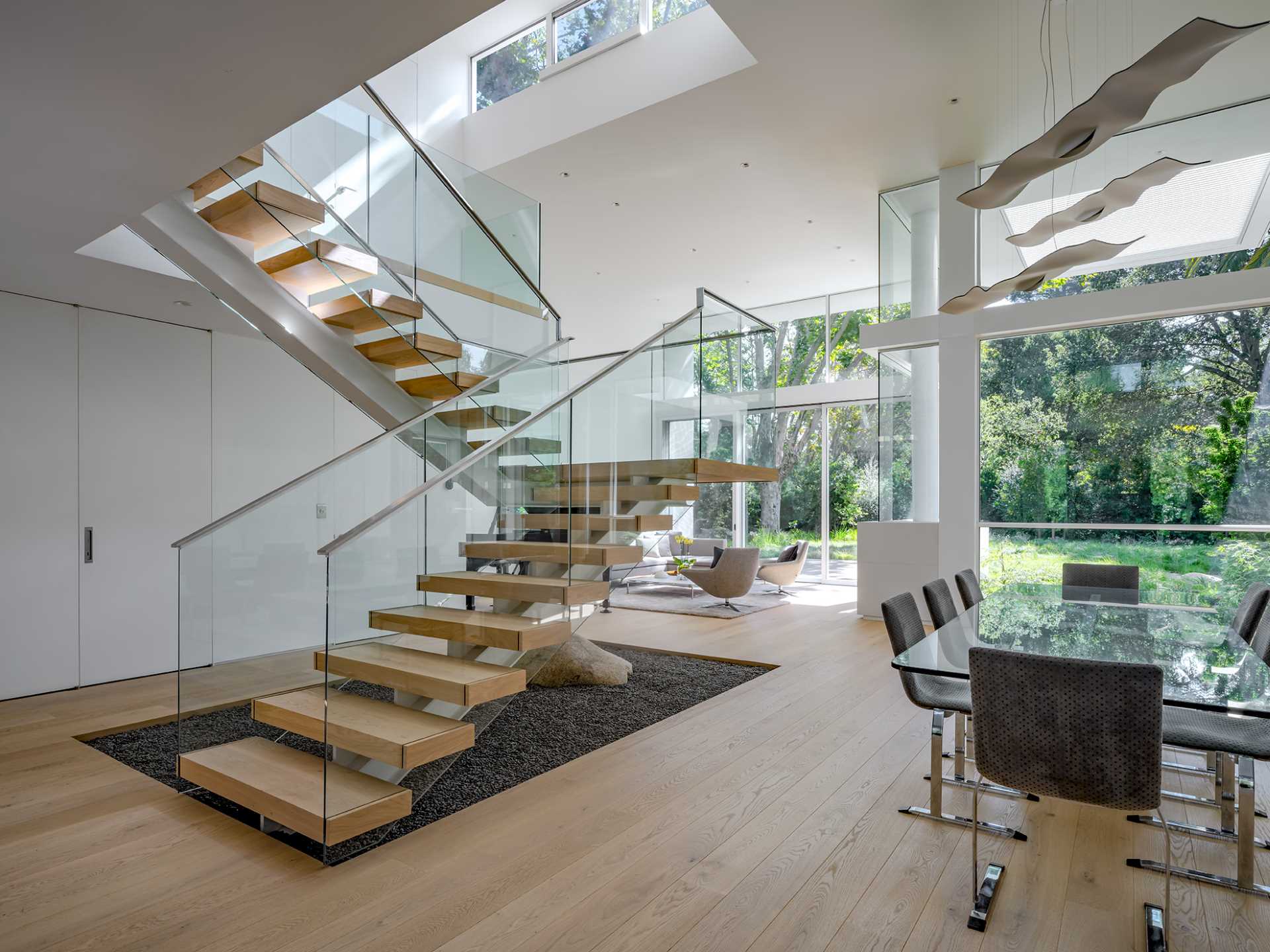 A free-standing, steel-framed stair is treated like a work of functional sculpture, hovering above an interior garden of gravel and a single boulder.