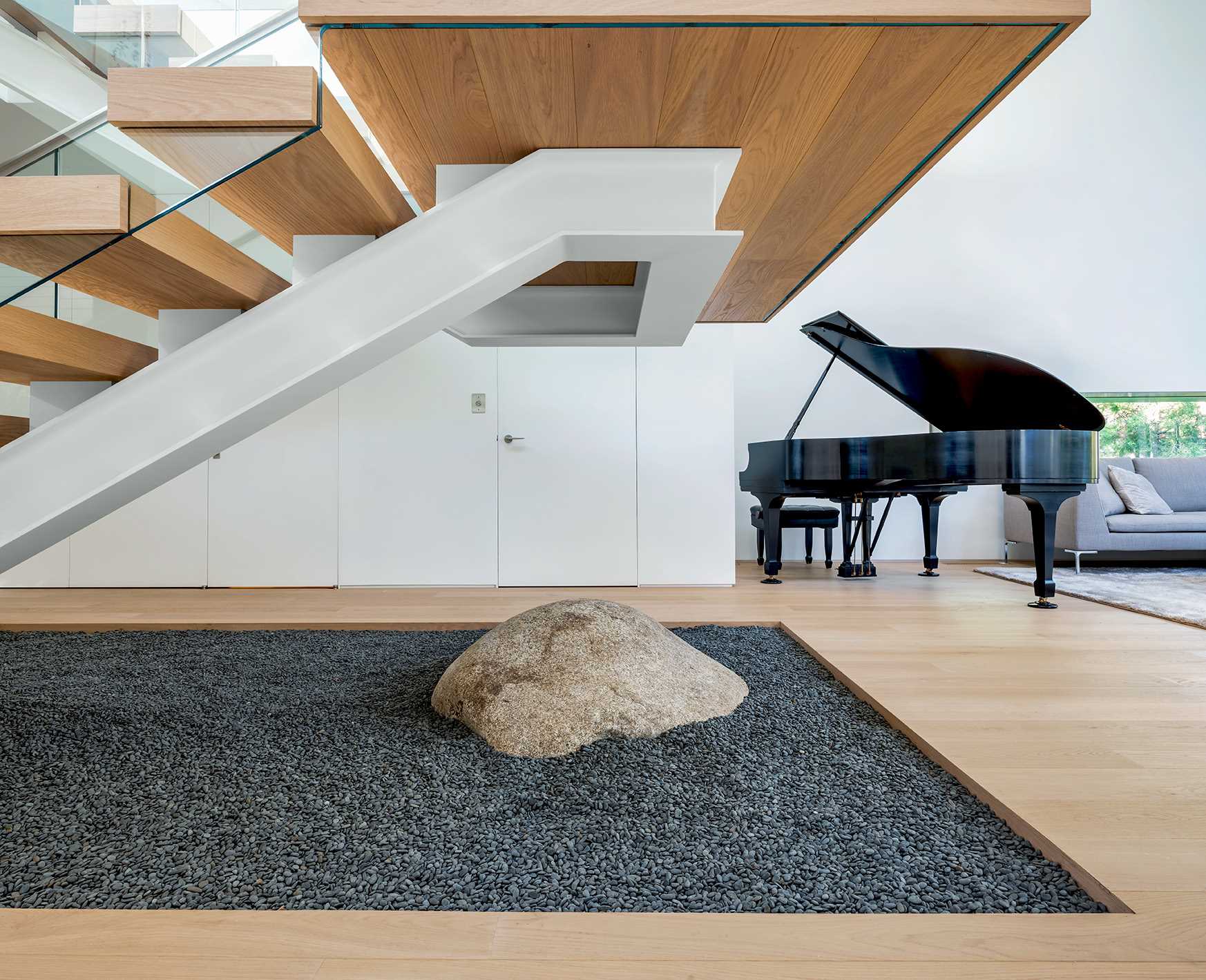 A free-standing, steel-framed stair is treated like a work of functional sculpture, hovering above an interior garden of gravel and a single boulder.