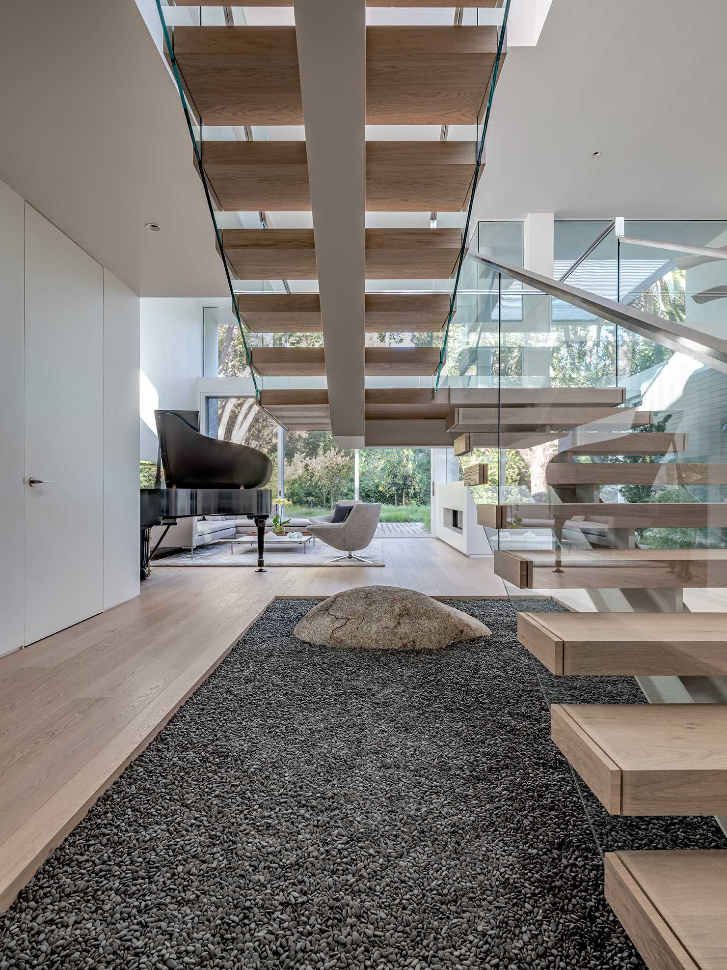 A free-standing, steel-framed stair is treated like a work of functional sculpture, hovering above an interior garden of gravel and a single boulder.