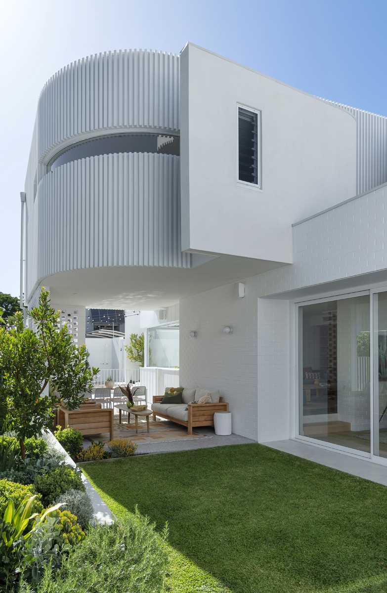 The rear of the home, with its curved design, creates a shaded space underneath that's been furnished as an outdoor lounge and dining area.