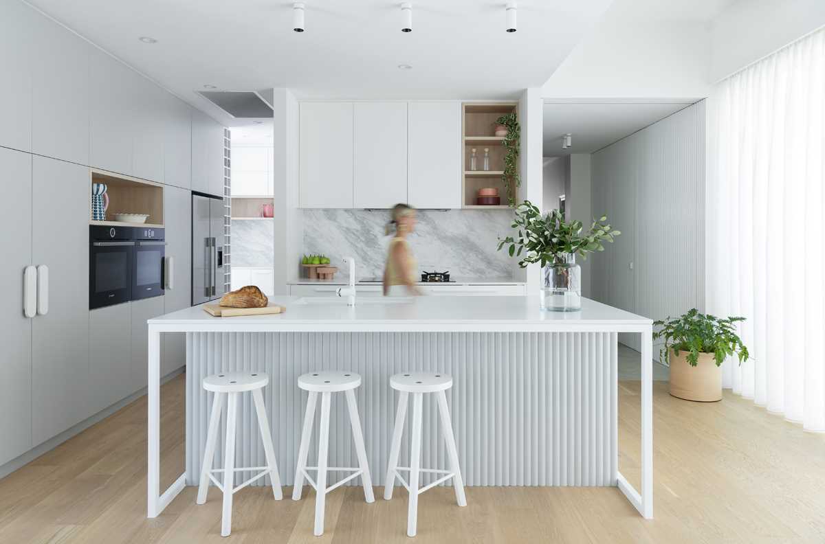 A modern kitchen with white and light grey cabinets, an island, and a small walk-in pantry area.