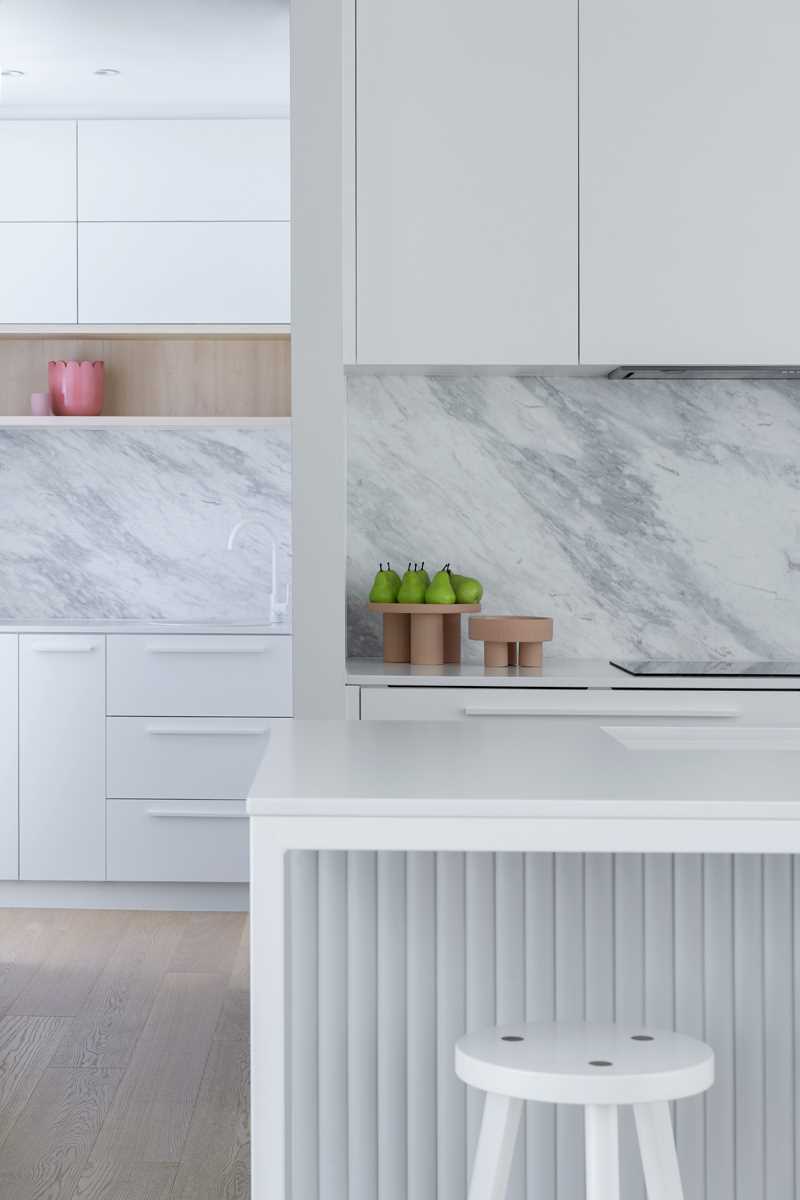 A modern kitchen with white and light grey cabinets, an island, and a small walk-in pantry area.