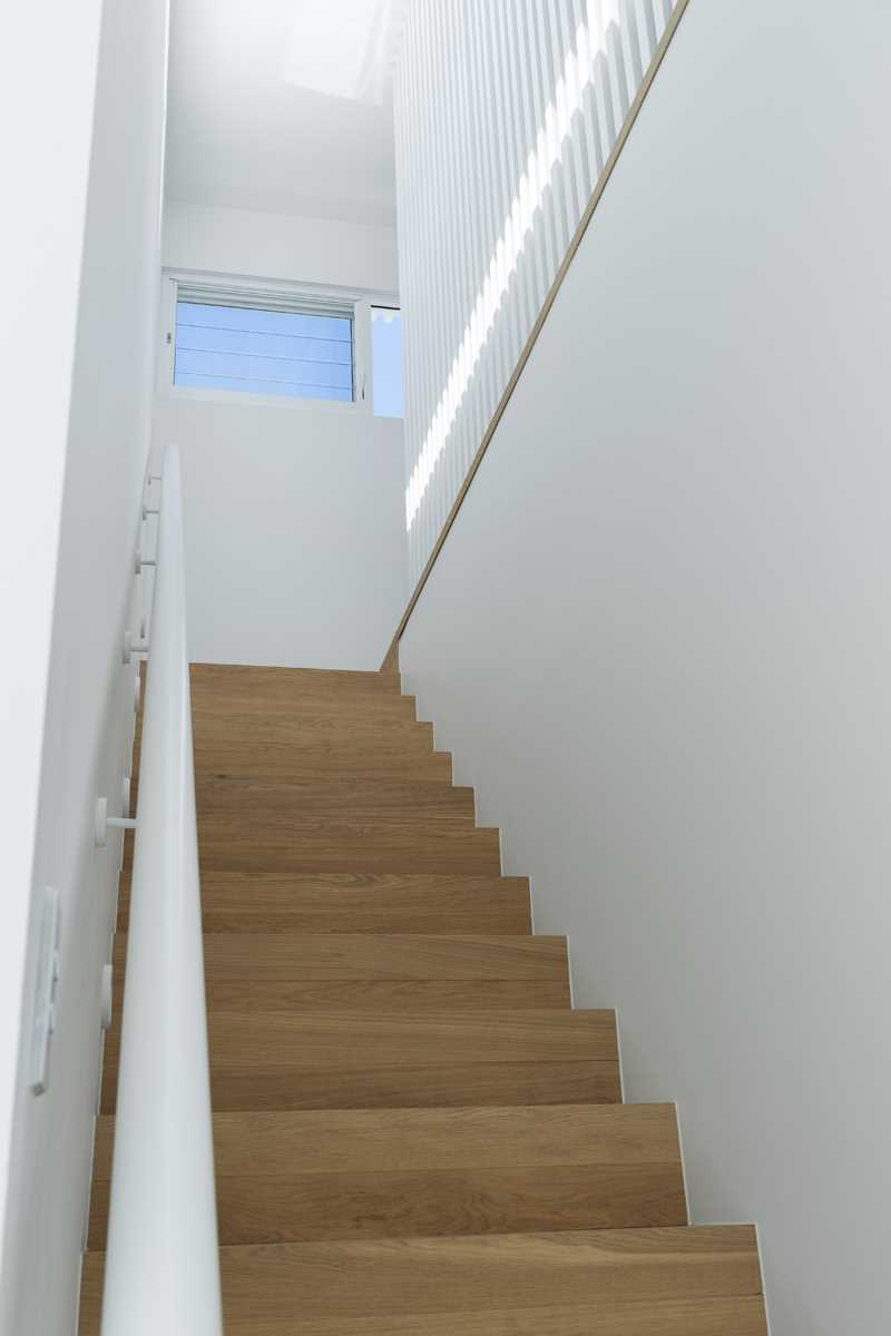 Wood stairs with white walls and railing connect the main level of the home with a pair of bedrooms and a study.