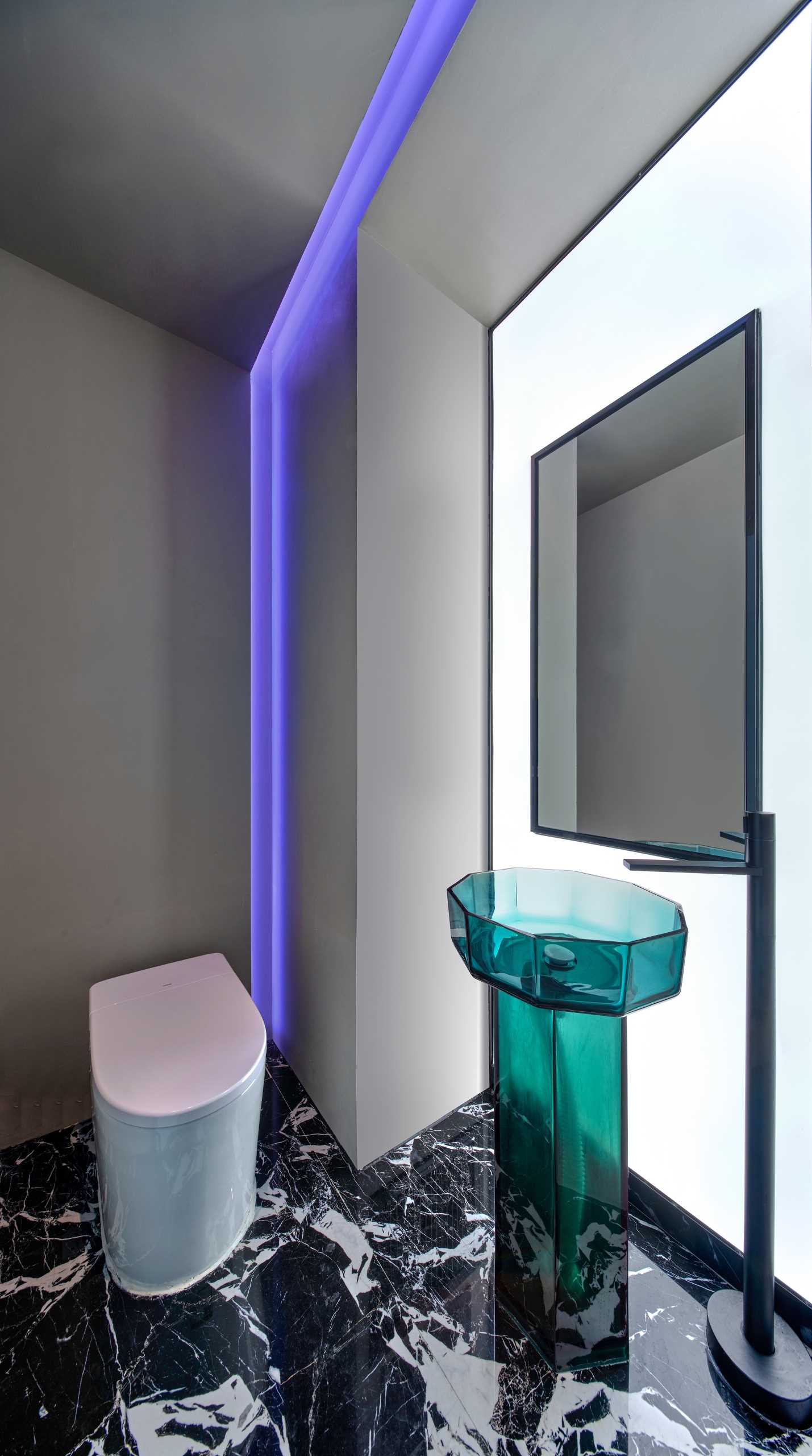 در حمام، نور بنفش LED وجود دارد که دیوار و یک حوض پایه شیشه ای سبز رنگ را می پوشاند.