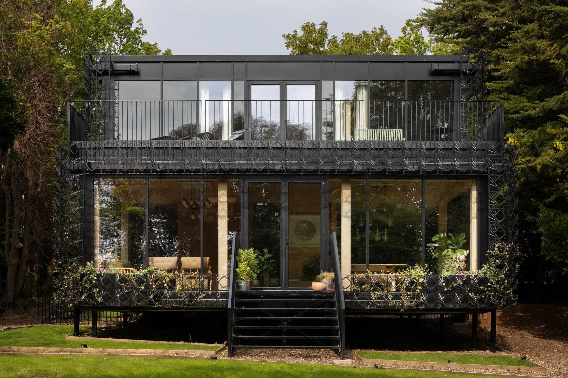 A modern black house with a sculptural facade designed to let plants grow on the exterior over time.