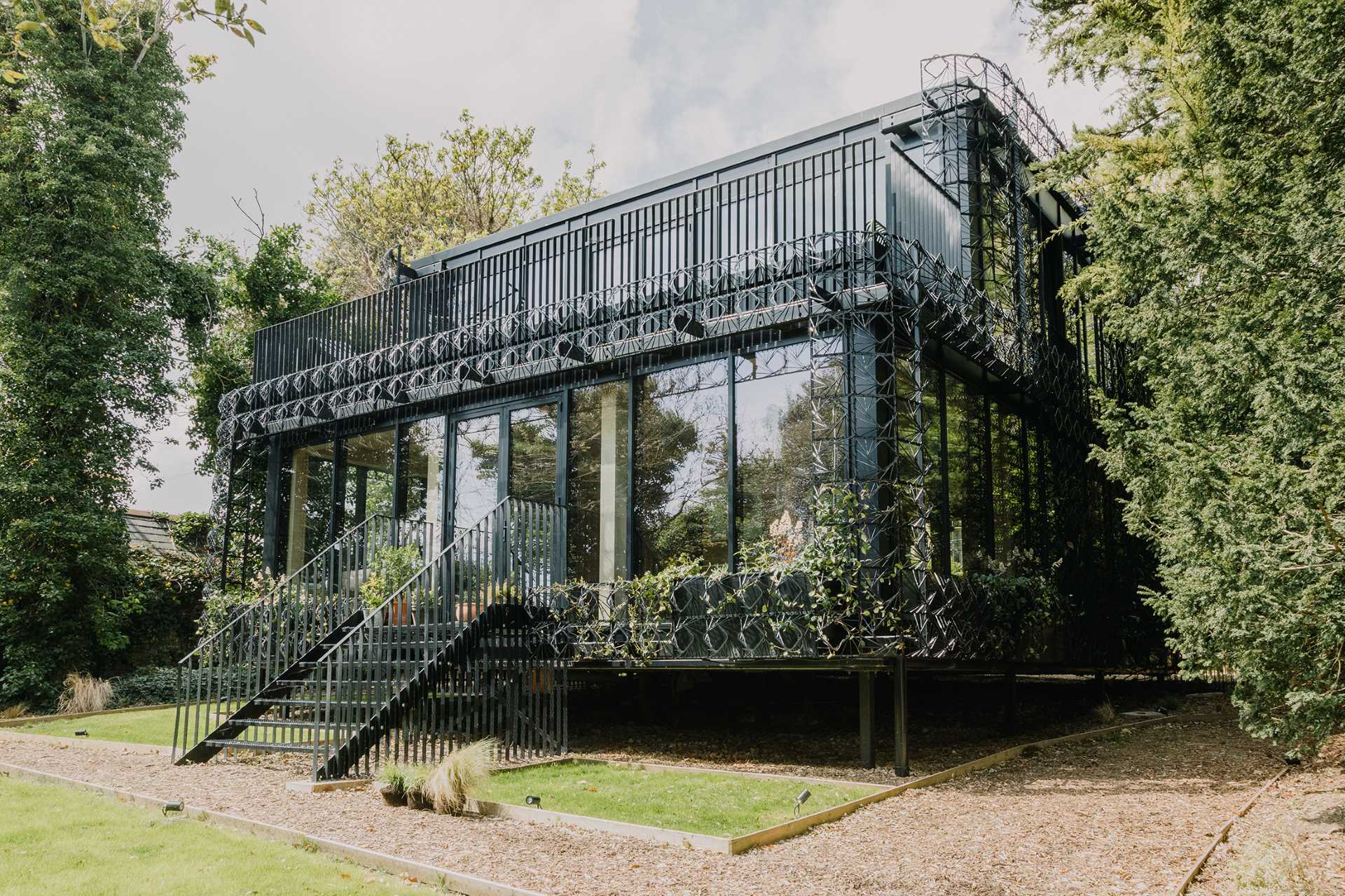 A modern black house with a sculptural facade designed to let plants grow on the exterior over time.