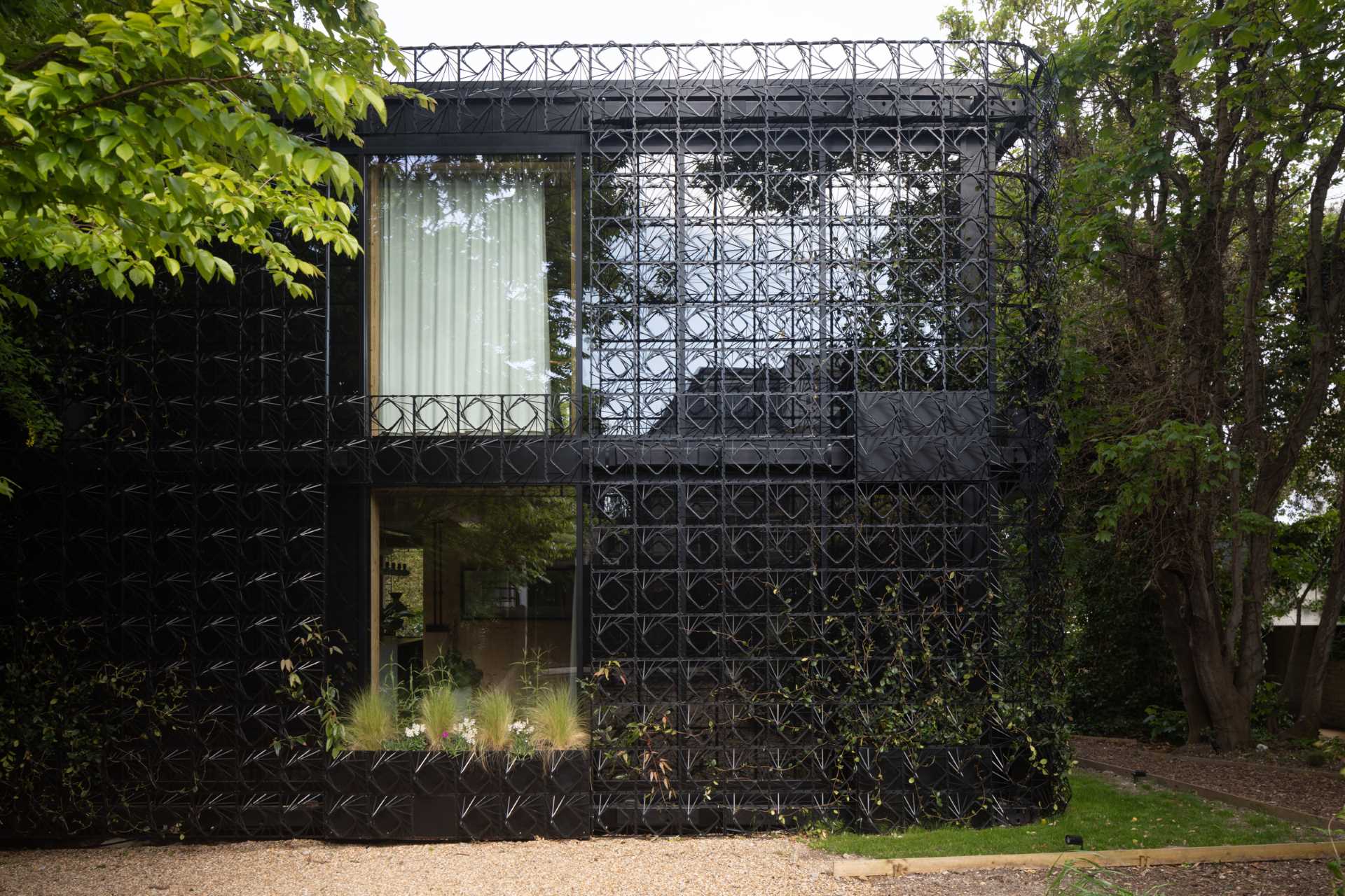 A modern black house with a sculptural facade designed to let plants grow on the exterior over time.
