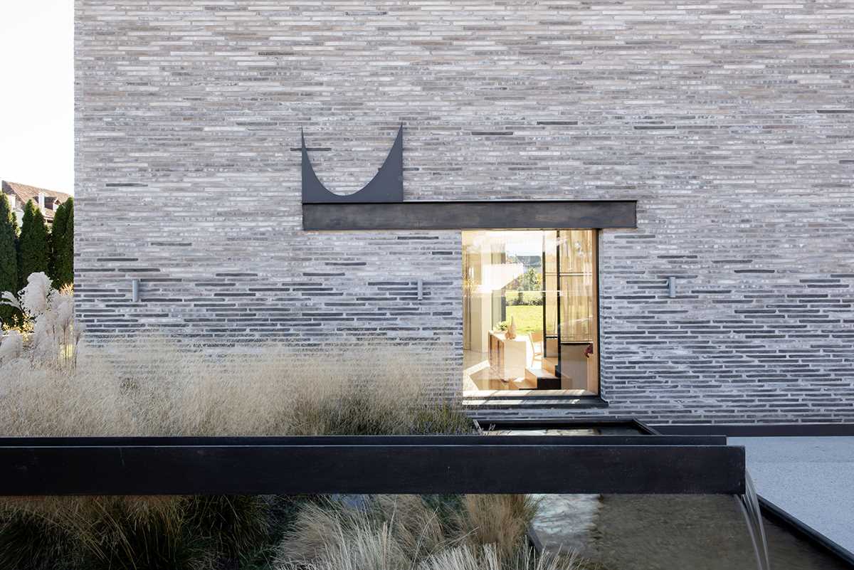 A modern home features handmade elongated bricks ranging from dark to light, and blackened steel channels sunk into the wall of the home.