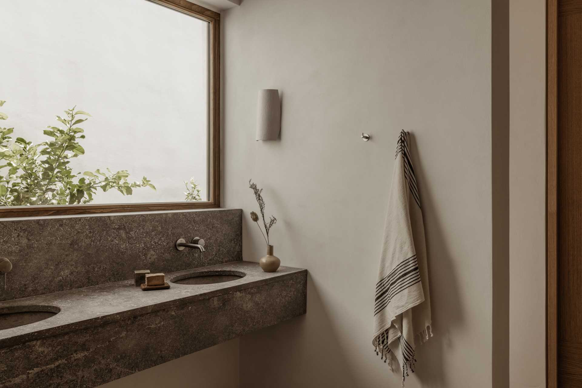 In this modern bathroom, a double vanity is located below a large window that provides natural light and views of the garden.