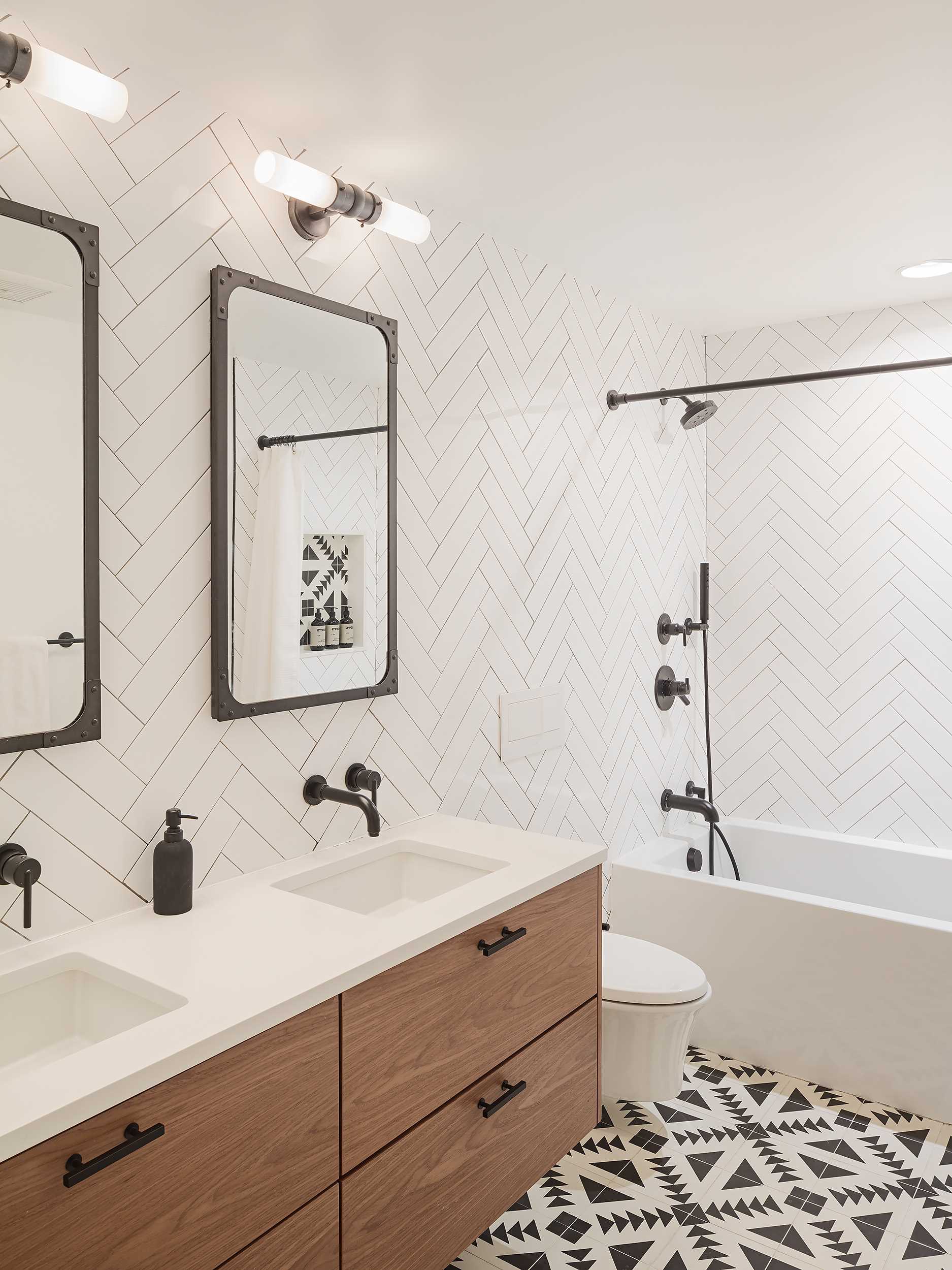 This remodeled guest bathroom has a new walnut floating vanity, herringbone wall tiles, and encaustic concrete floor tiles.