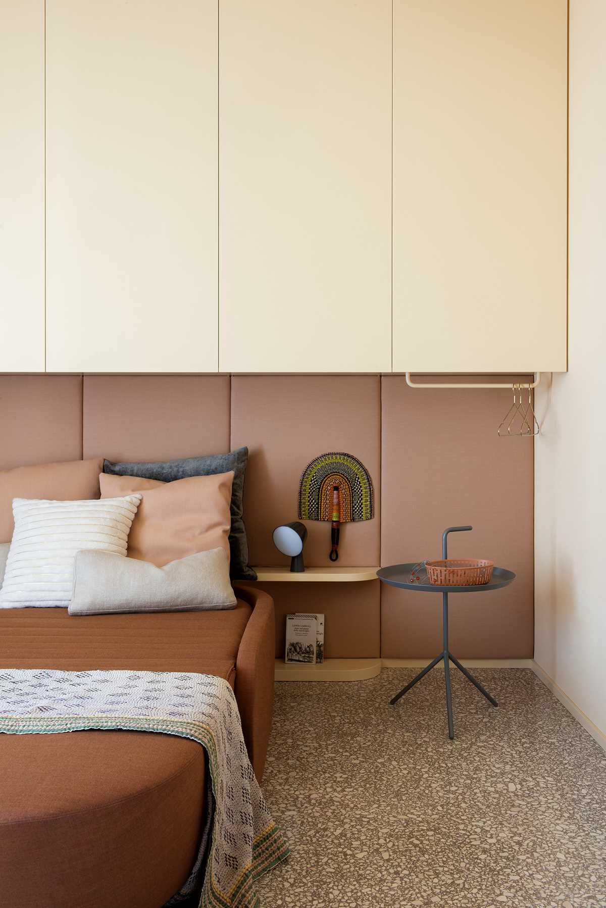 In this modern bedroom, an upholstered headboard lines the wall, while cabinets are located above the bed.