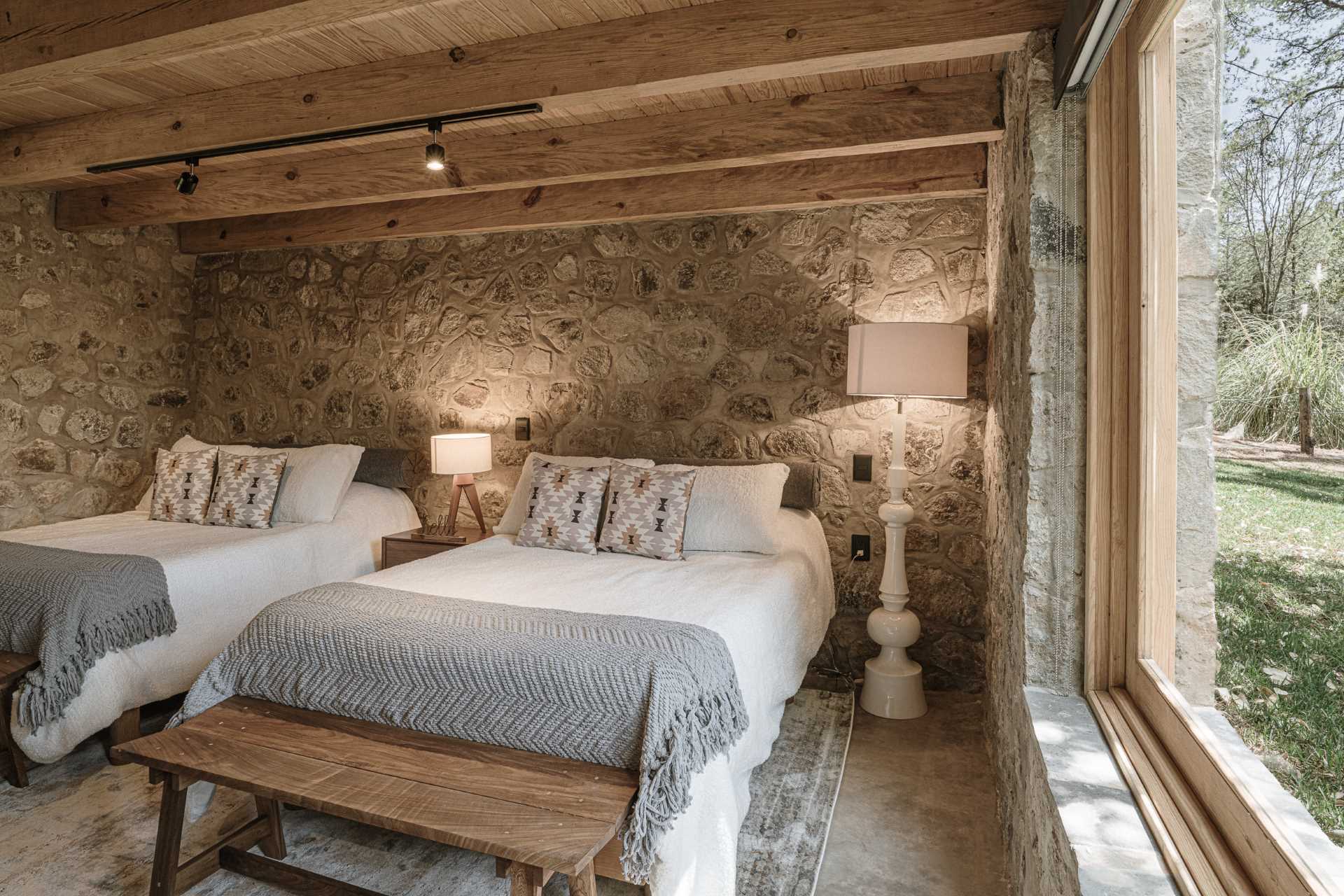 A modern stone and wood bedroom with two beds and built-in cabinetry.