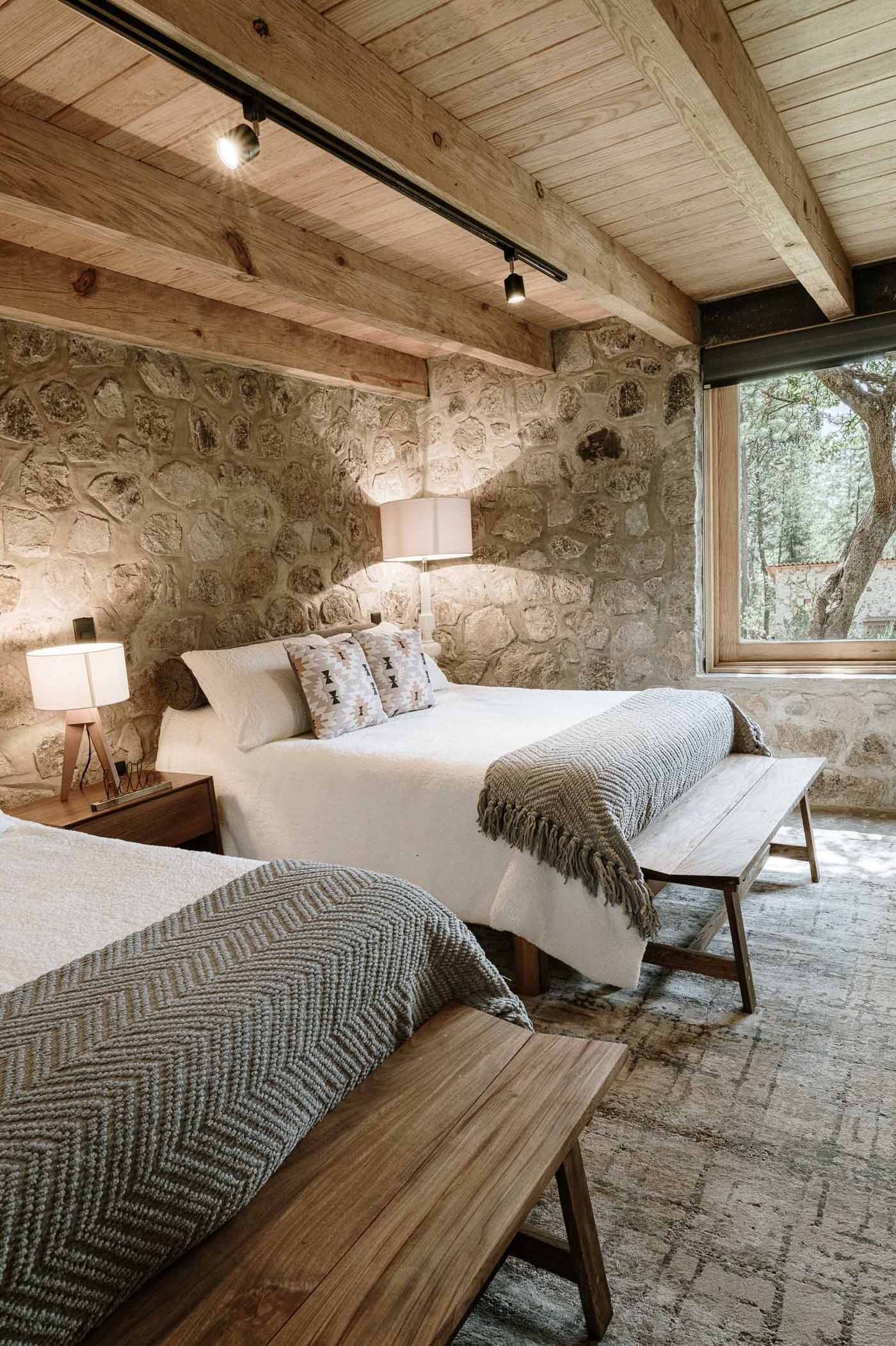 A modern stone and wood bedroom with two beds and built-in cabinetry.