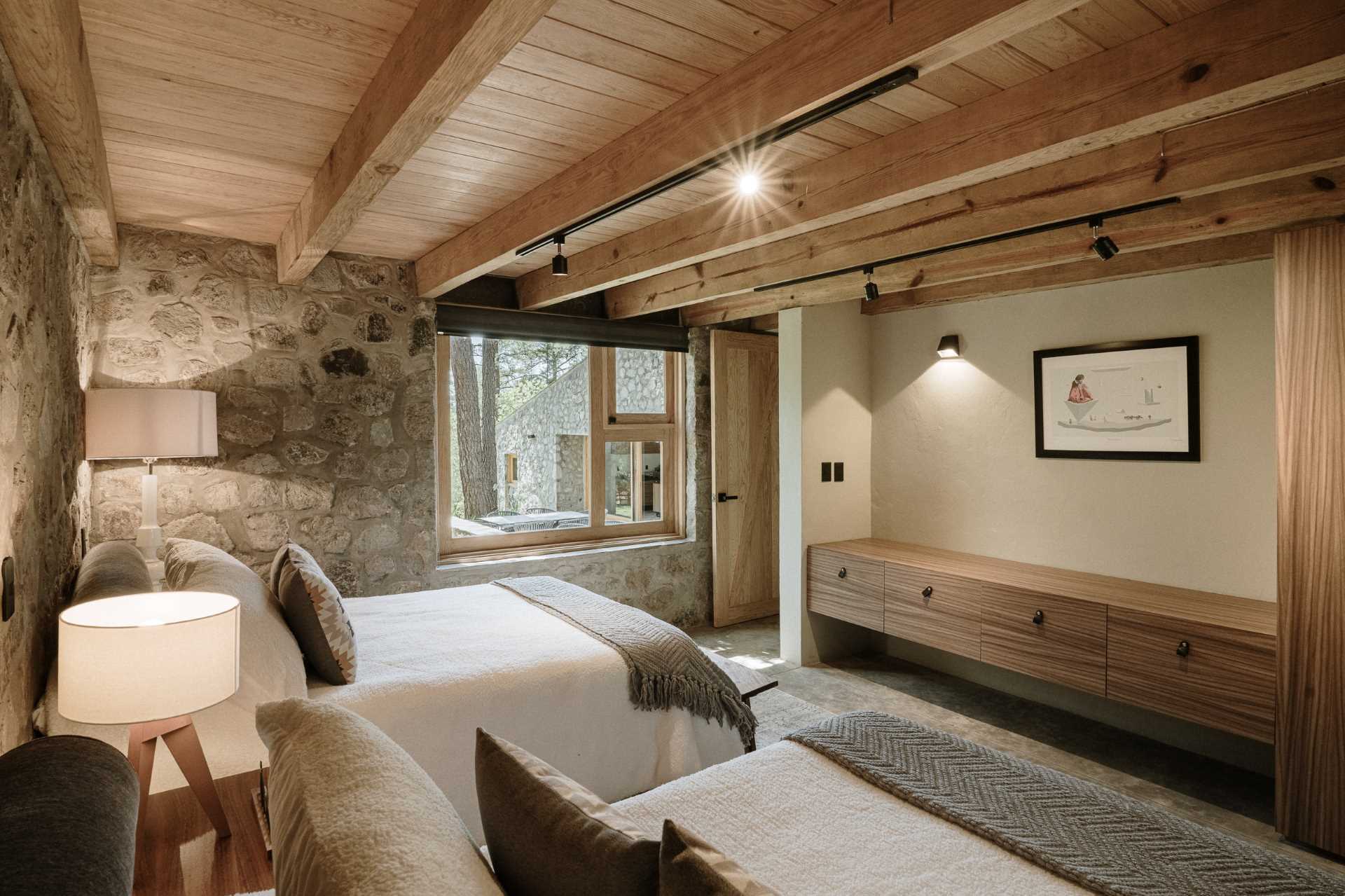 A modern stone and wood bedroom with two beds and built-in cabinetry.