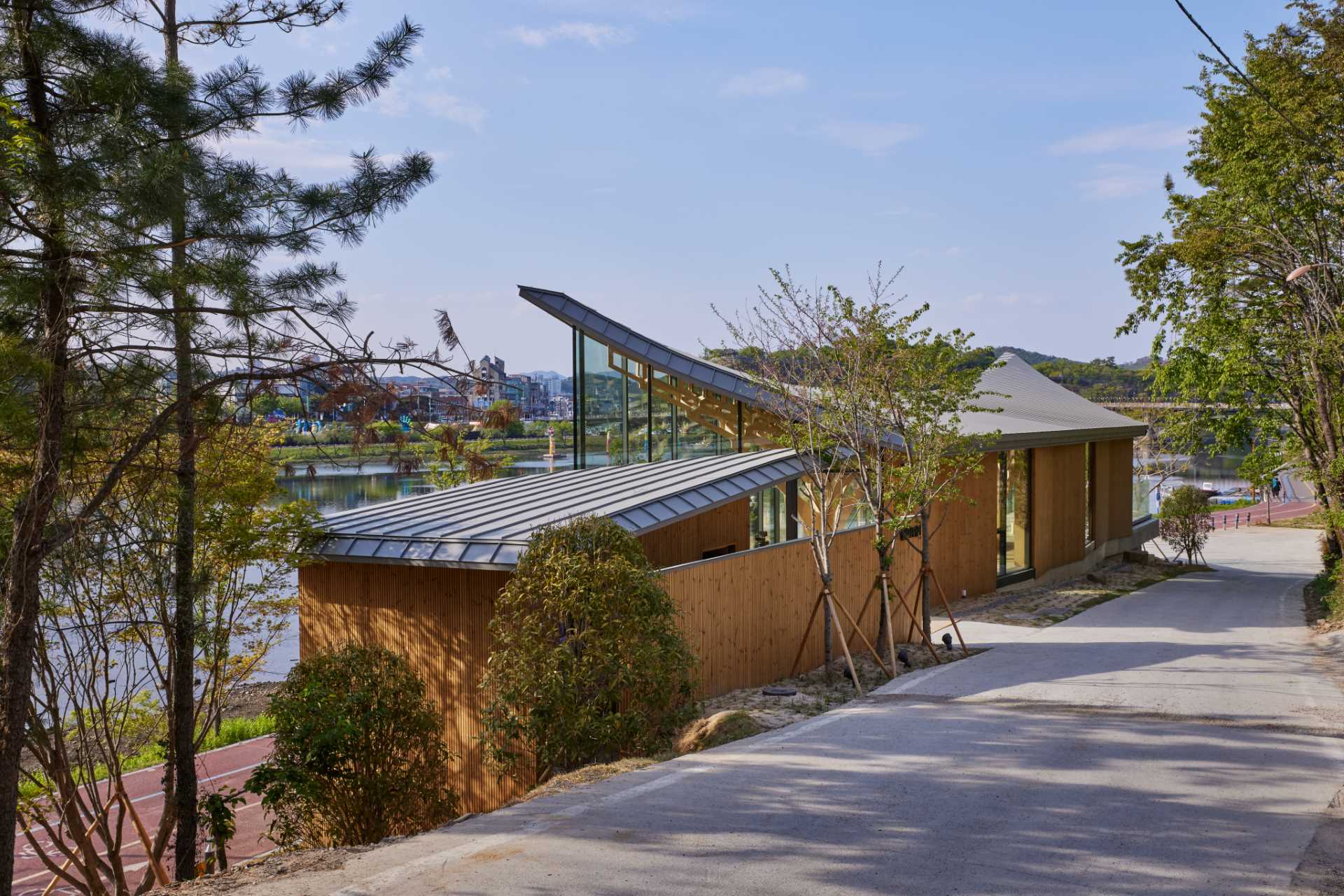 Six tree-like columns showcase wood craftsmanship inside a riverside pavilion with a glass front.