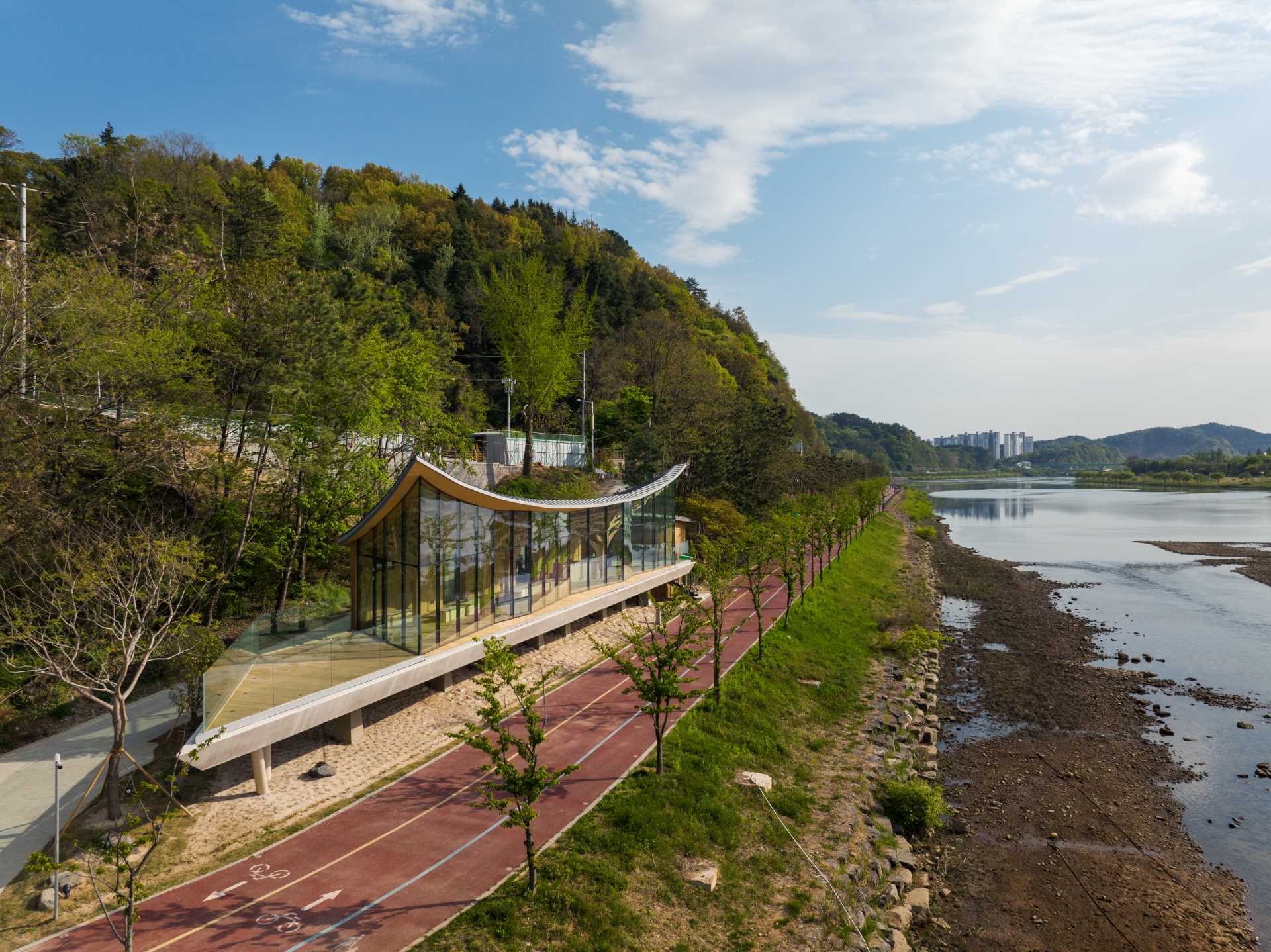 Six tree-like columns showcase wood craftsmanship inside a riverside pavilion with a glass front.