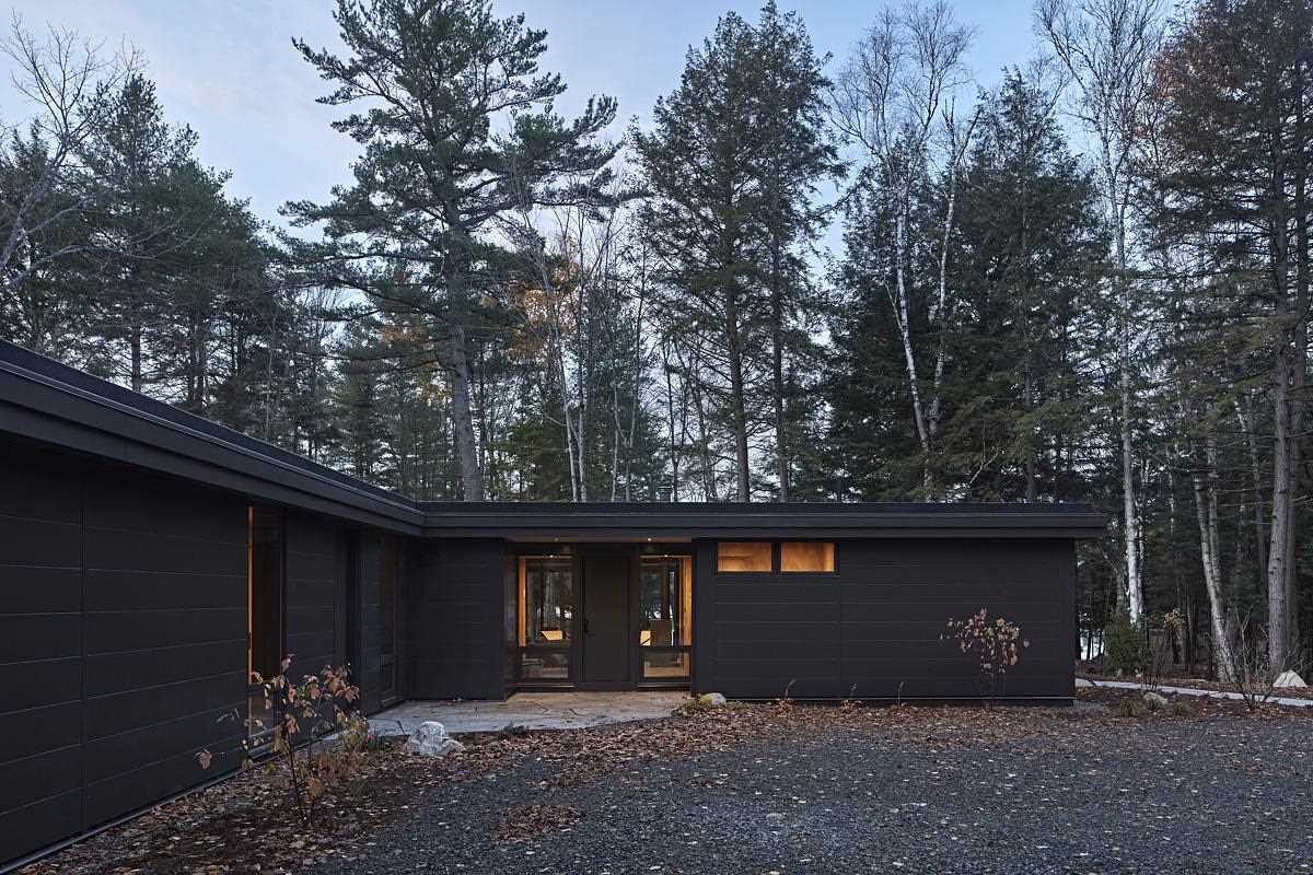 A modern L-shaped cottage with black exterior and large roof overhangs.