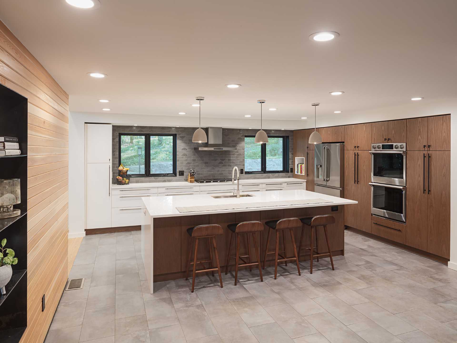 This modern kitchen includes a combination of walnut tall cabinets and matte white base cabinets that provide ample space for cooking and entertaining, with the large island separating the kitchen from the dining area.