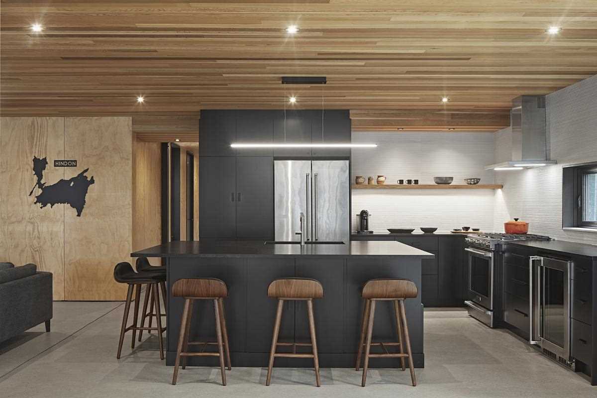A modern black kitchen with wood ceiling and concrete floor.