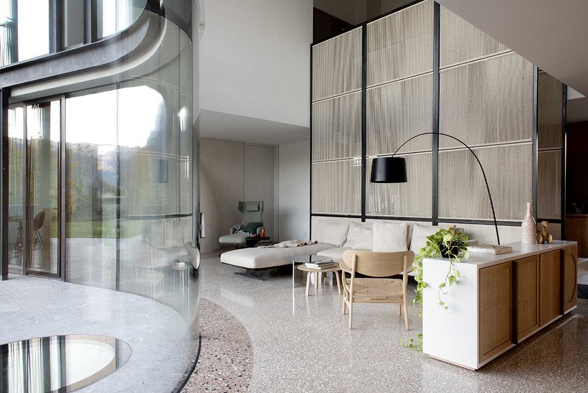 A modern living room with a double-height ceiling and curved glass windows.