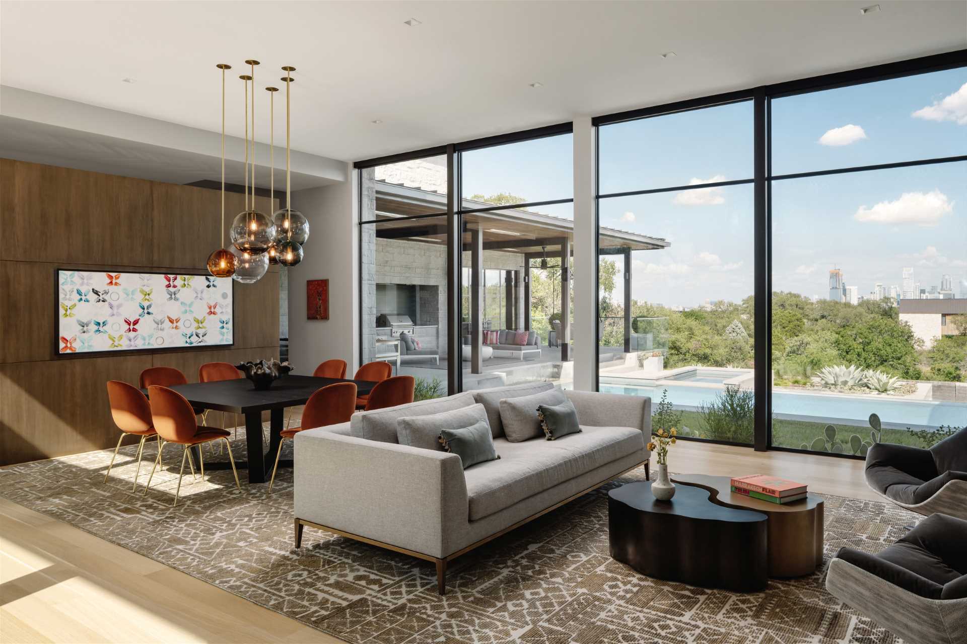 The main social areas of this modern home, like the living room, dining area, and kitchen, run parallel to the pool, while the primary suite and game room anchor these spaces to either side