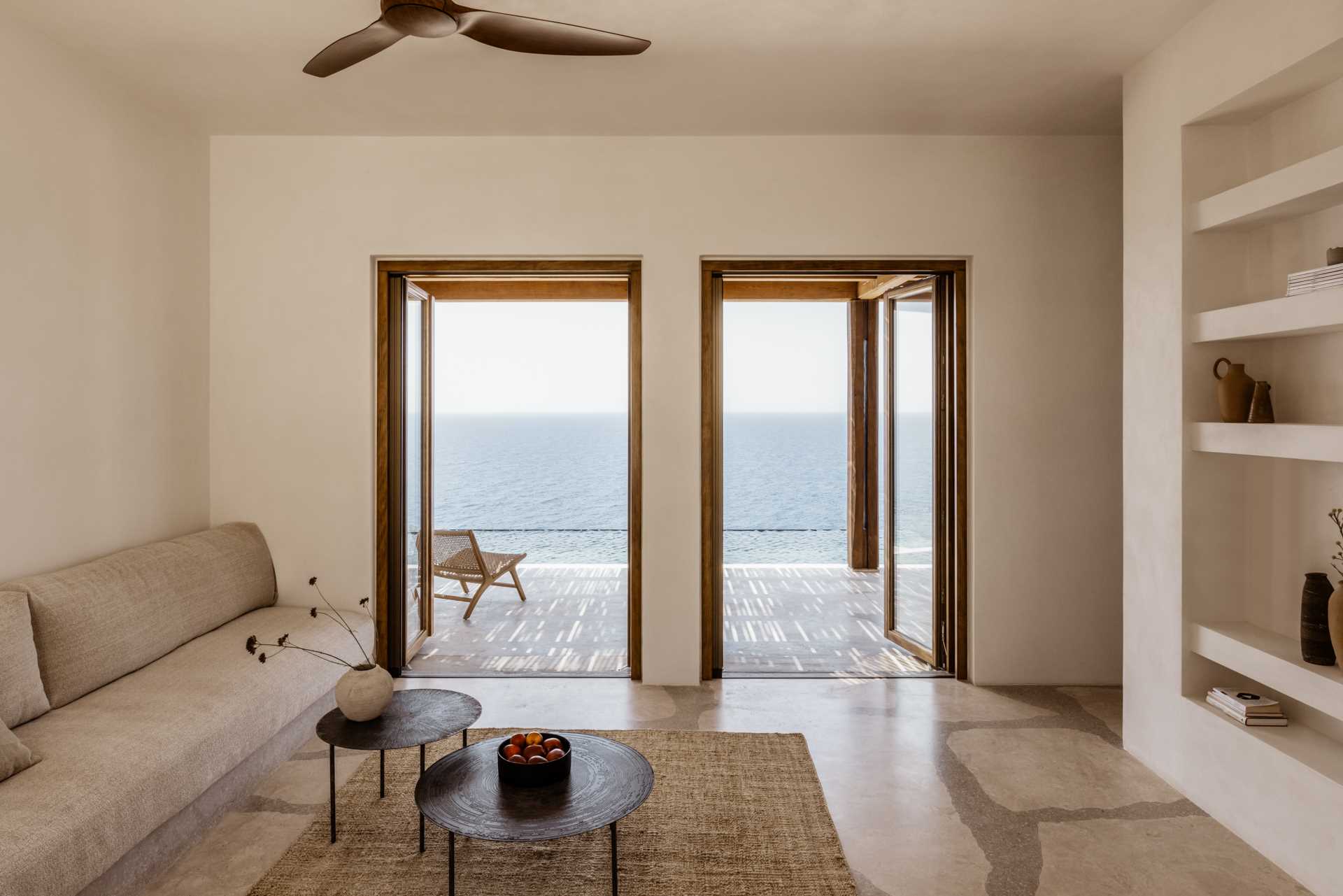 A modern living room with a neutral color and material palette, and built-in shelving and doors that open to a terrace.