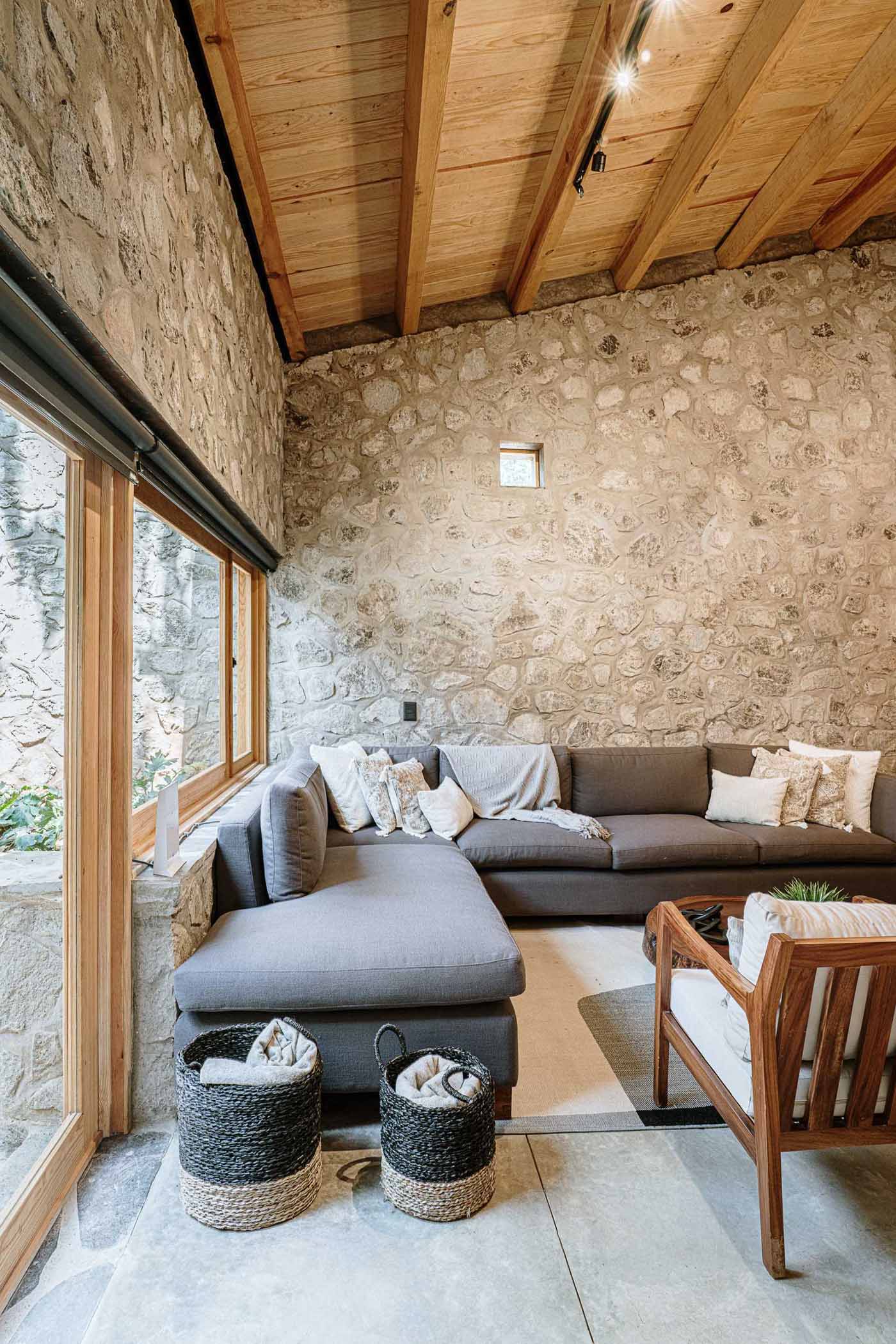 A modern living room with an L-shaped couch that lines the corner and wood stairs that lead to a lofted bedroom.