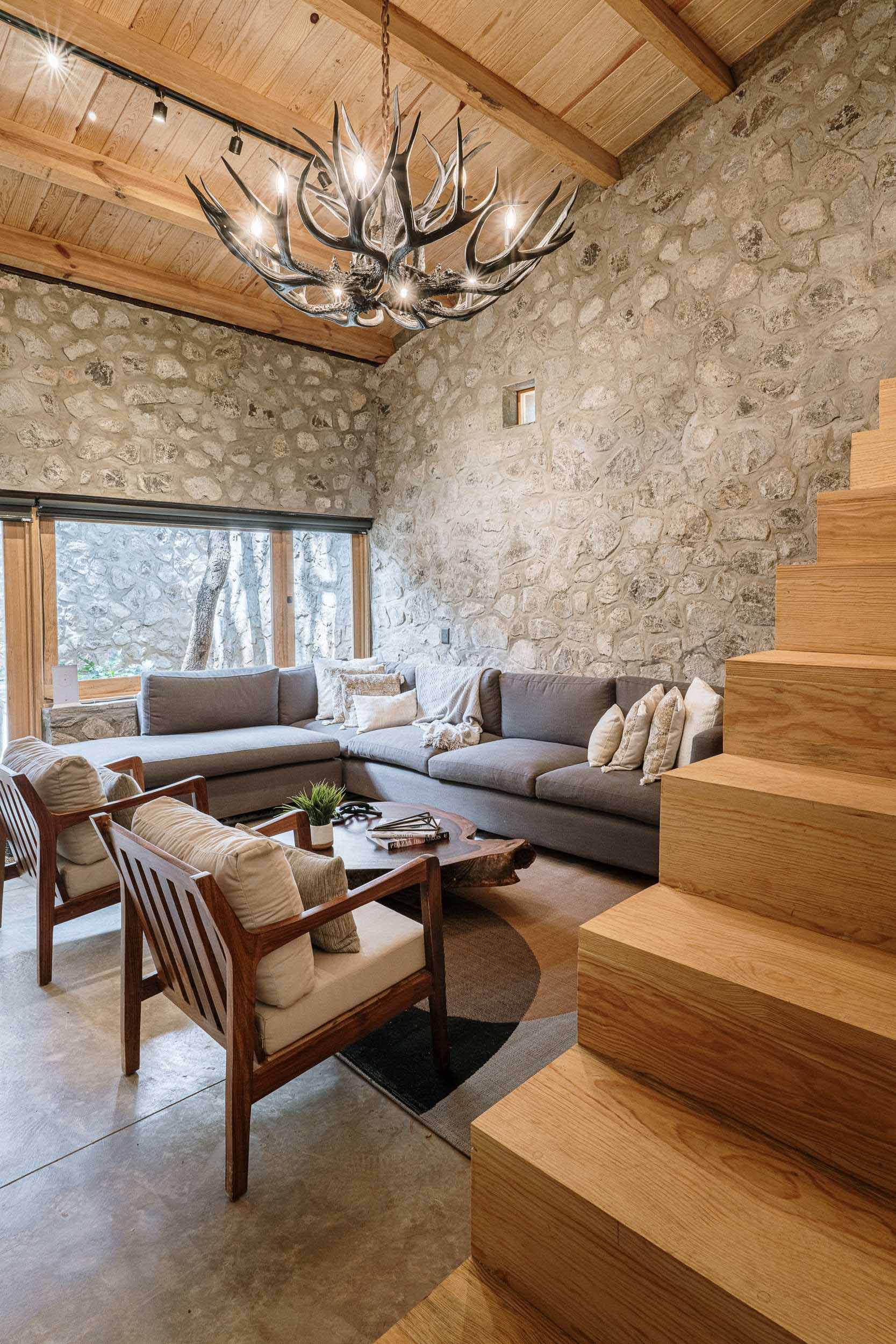 A modern living room with an L-shaped couch that lines the corner and wood stairs that lead to a lofted bedroom.