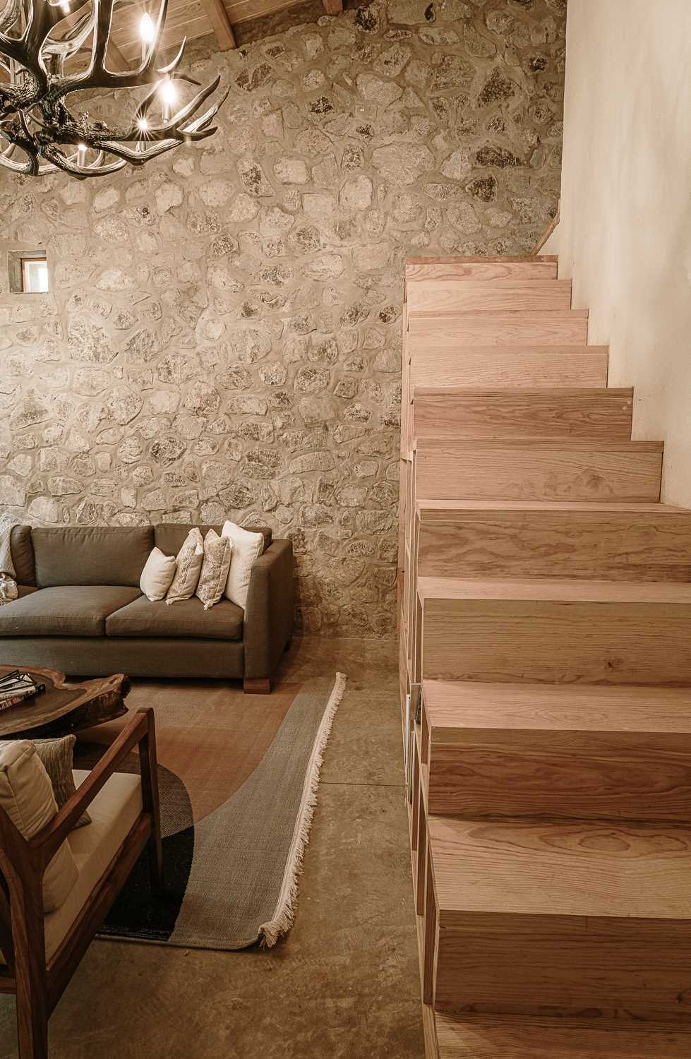 A modern living room with an L-shaped couch that lines the corner and wood stairs that lead to a lofted bedroom.