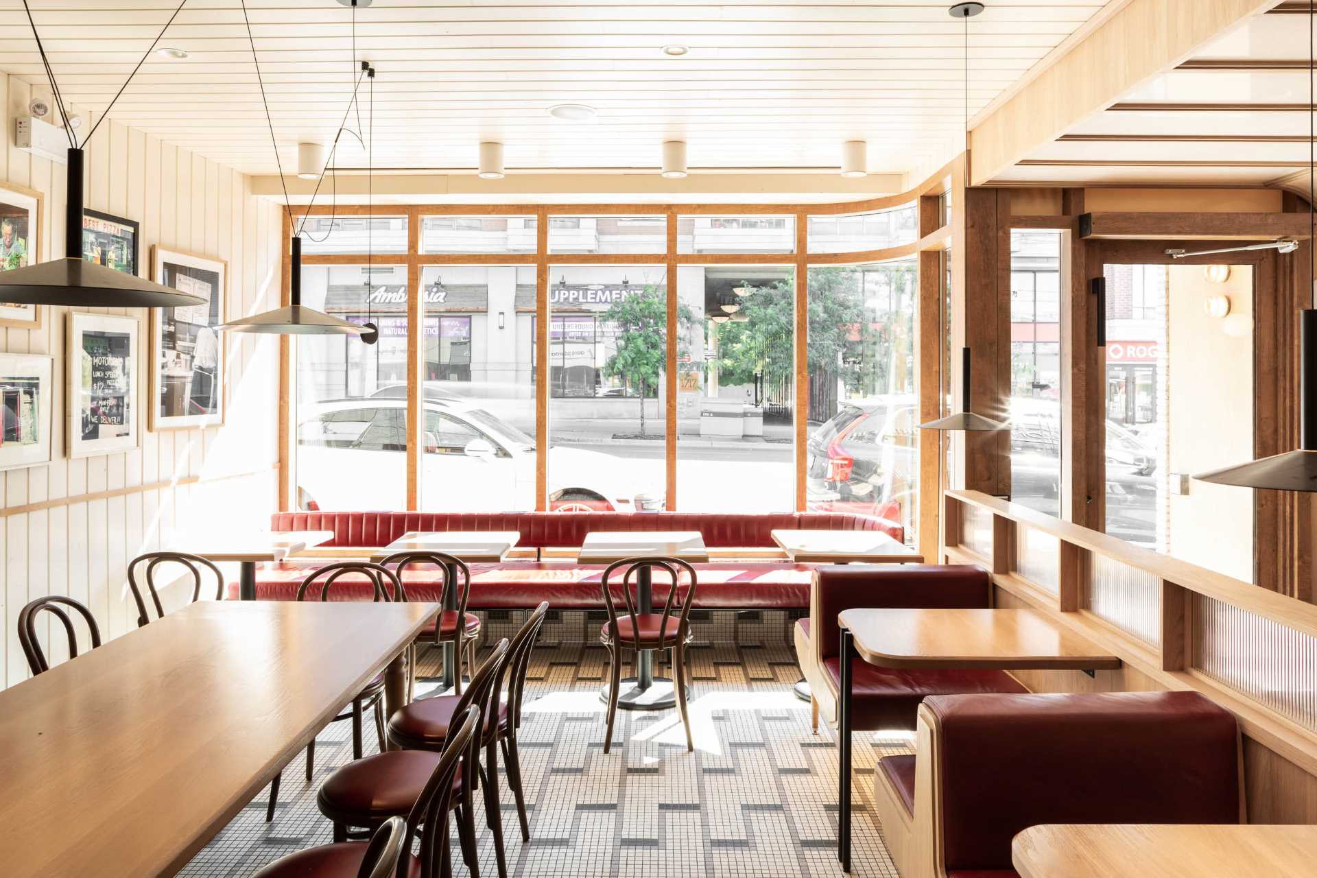 A modern pizzeria that features tile floor, banquette seating, a farm table, and a wall of shelving.