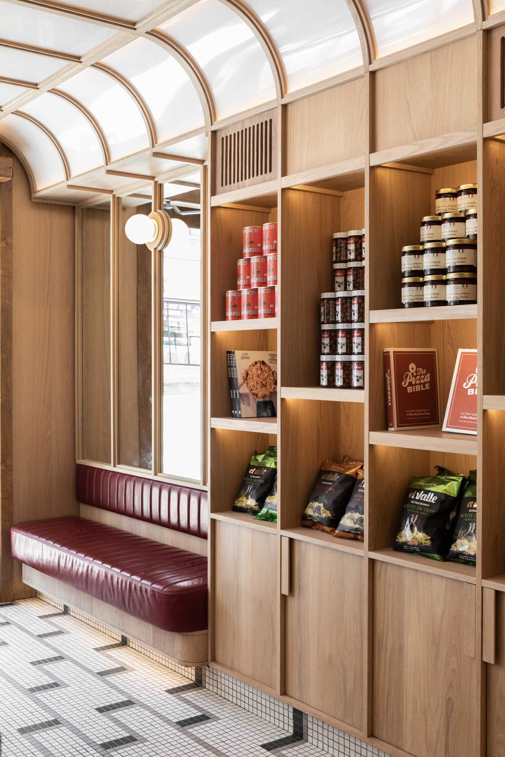 A modern pizzeria that features tile floor, banquette seating, a farm table, and a wall of shelving.