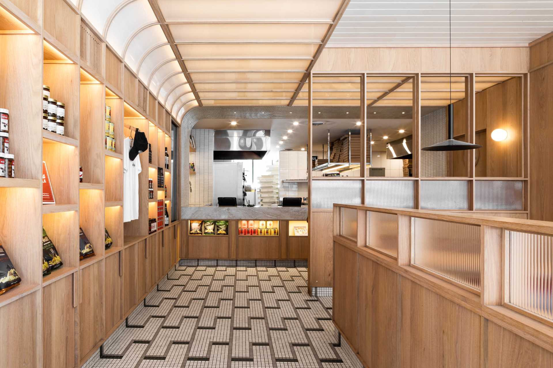 A modern pizzeria that features tile floor, banquette seating, a farm table, and a wall of shelving.