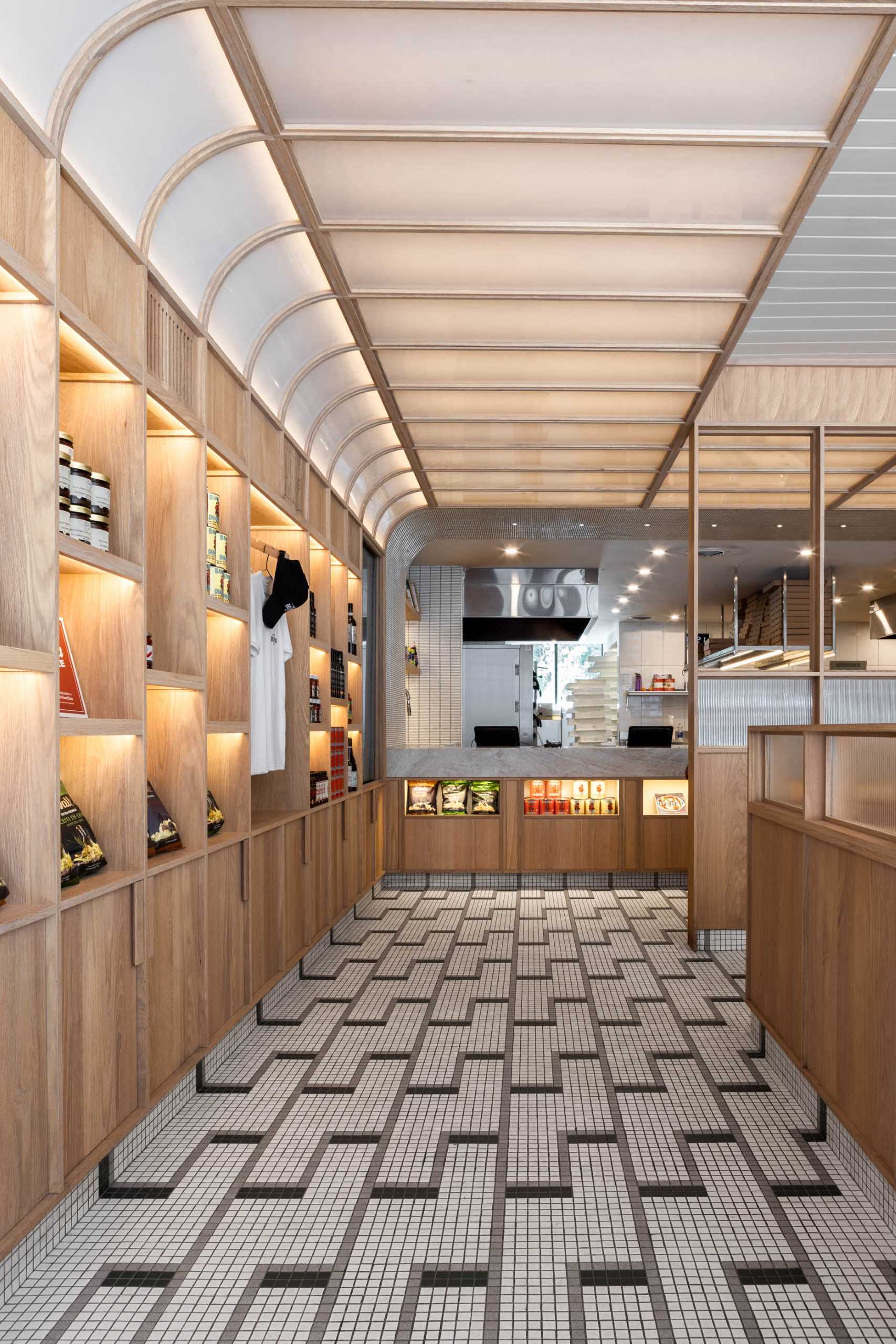 A modern pizzeria that features tile floor, banquette seating, a farm table, and a wall of shelving.