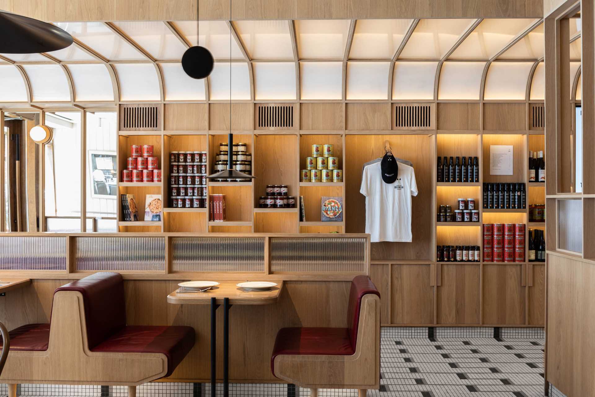 A modern pizzeria that features tile floor, banquette seating, a farm table, and a wall of shelving.