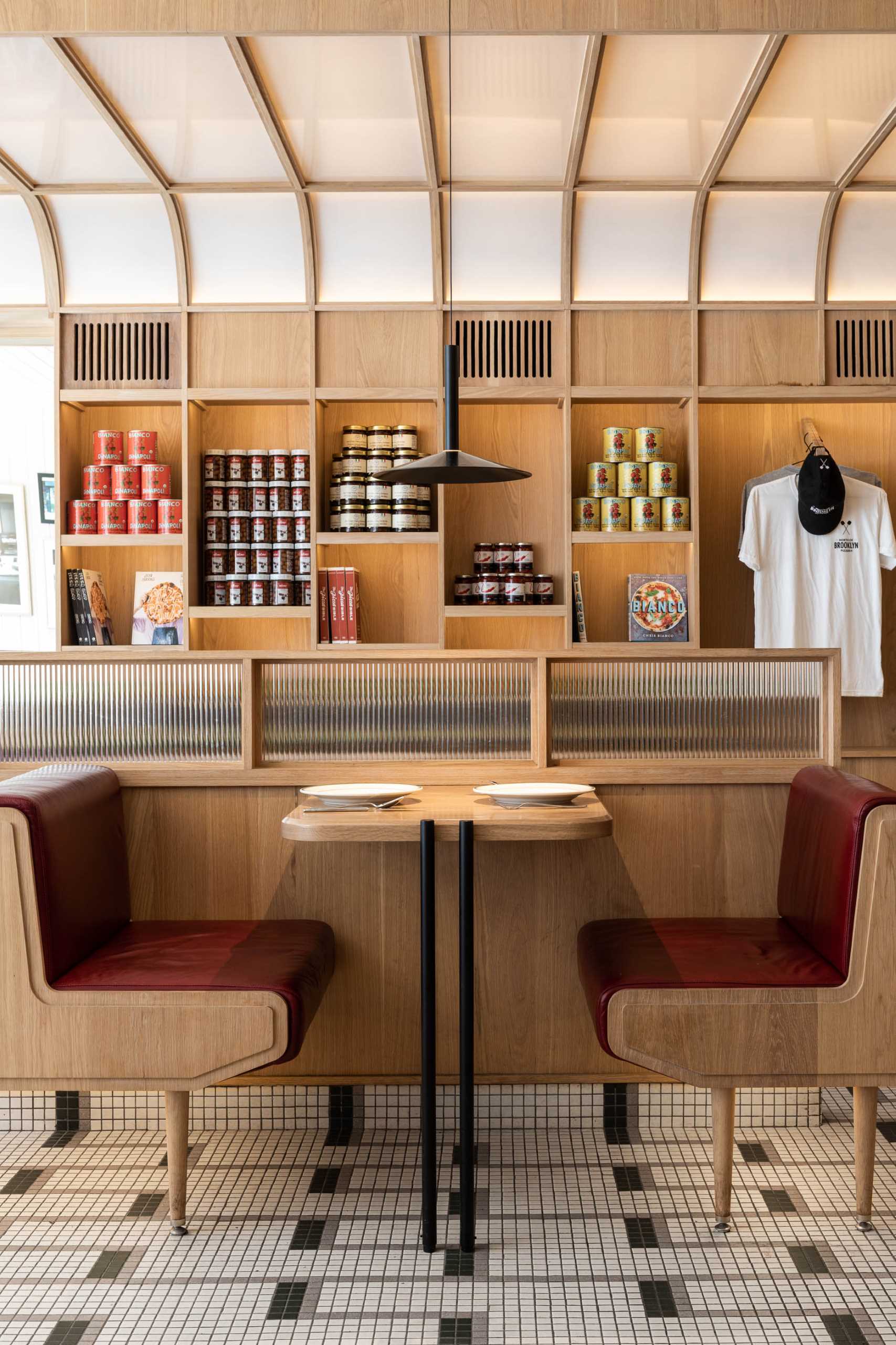 A modern pizzeria that features tile floor, banquette seating, a farm table, and a wall of shelving.