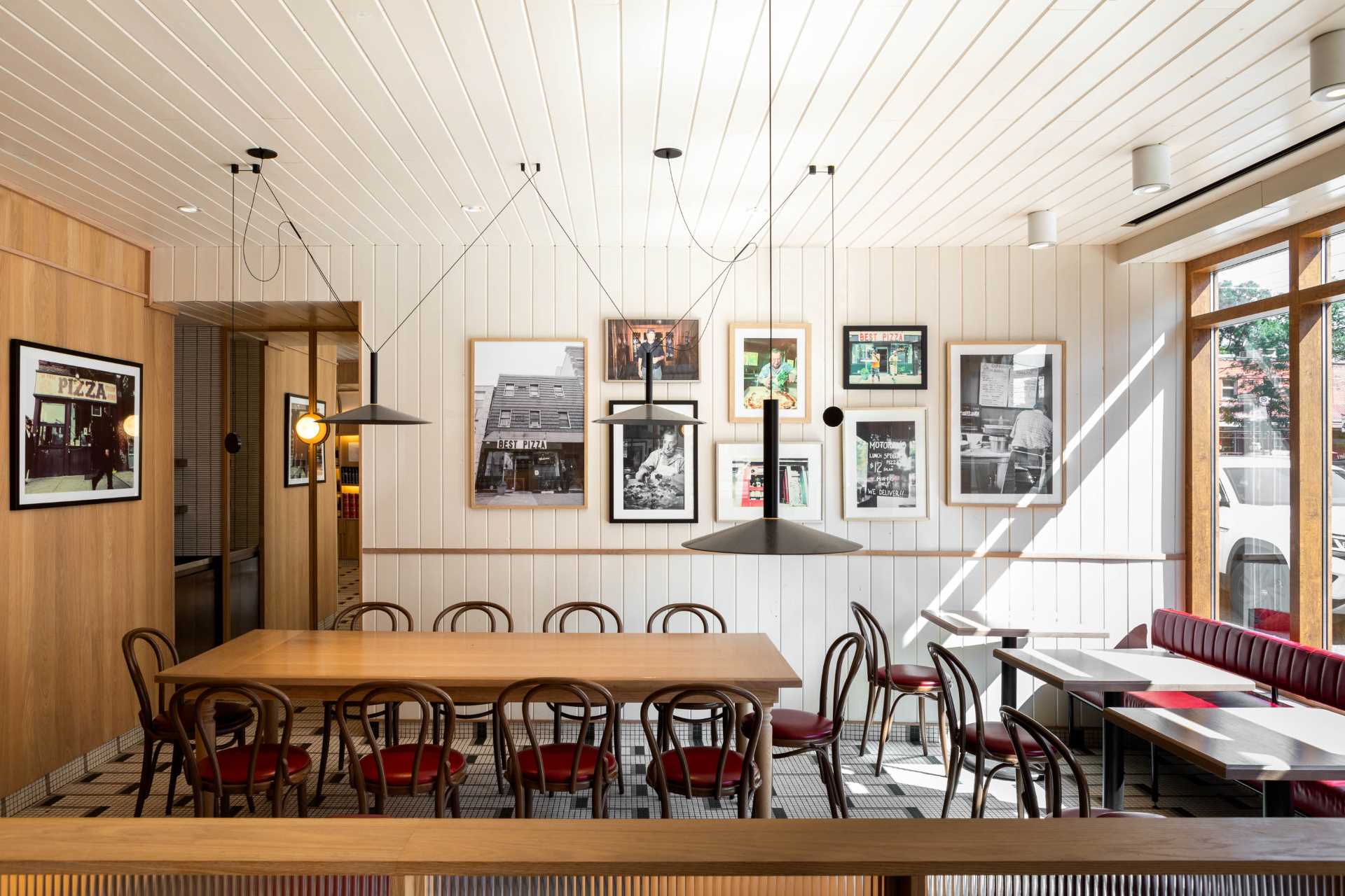 A modern pizzeria that features tile floor, banquette seating, a farm table, and a wall of shelving.