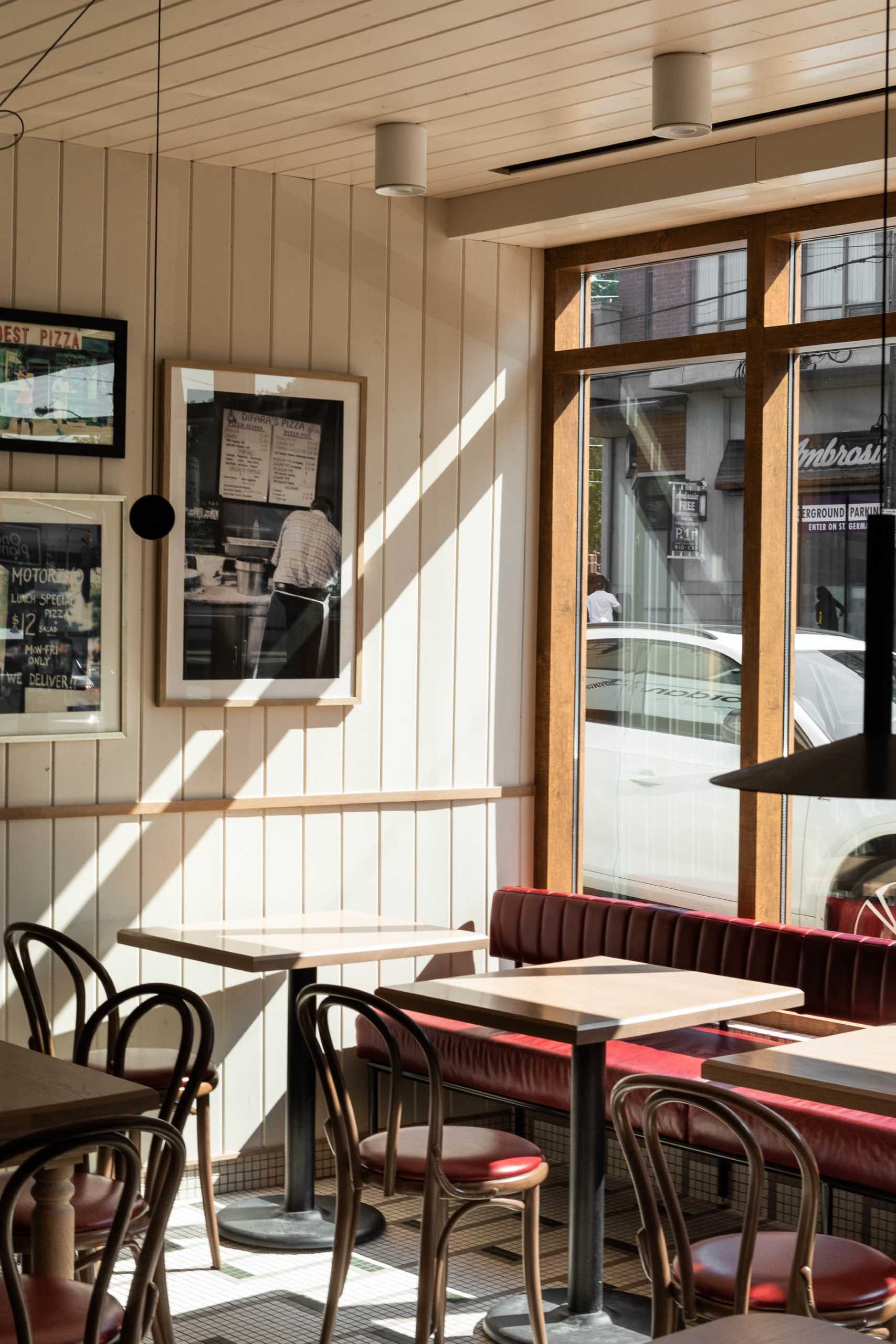 A modern pizzeria that features tile floor, banquette seating, a farm table, and a wall of shelving.