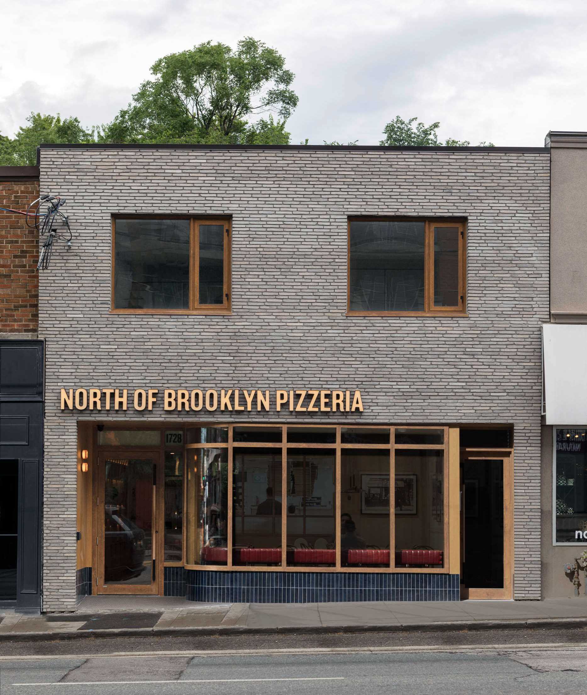 نمای این پیتزا فروشی دگرگون شده و دارای آجر روشن، پنجره های چوبی و کاشی سرامیک آبی منحنی است.
