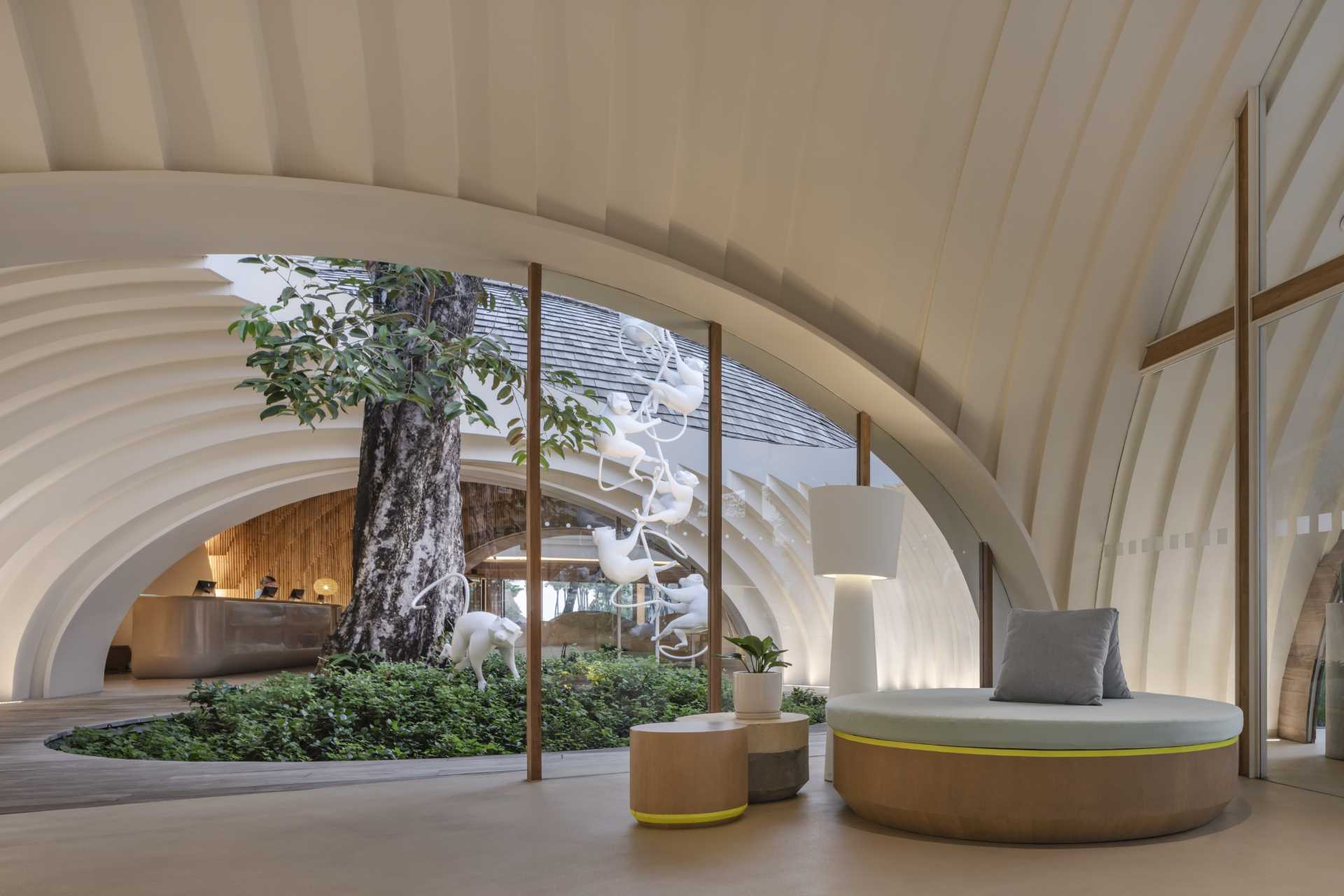 A modern hotel lobby is designed around an existing Java Plum tree with an oculus framing the sky.