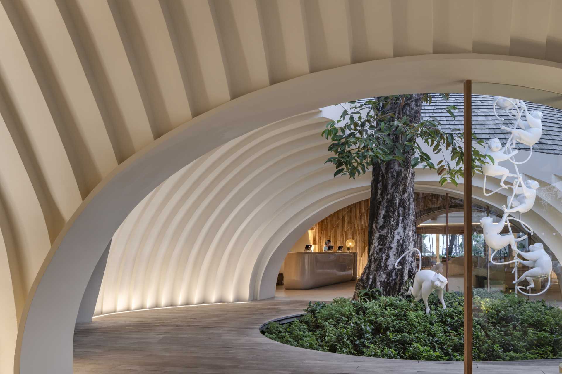 A modern hotel lobby is designed around an existing Java Plum tree with an oculus framing the sky.