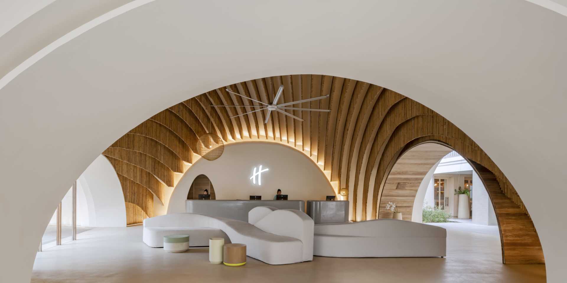 A modern hotel lobby that includes curved walls, hanging planes of bamboo, and hidden lighting that highlights the design.