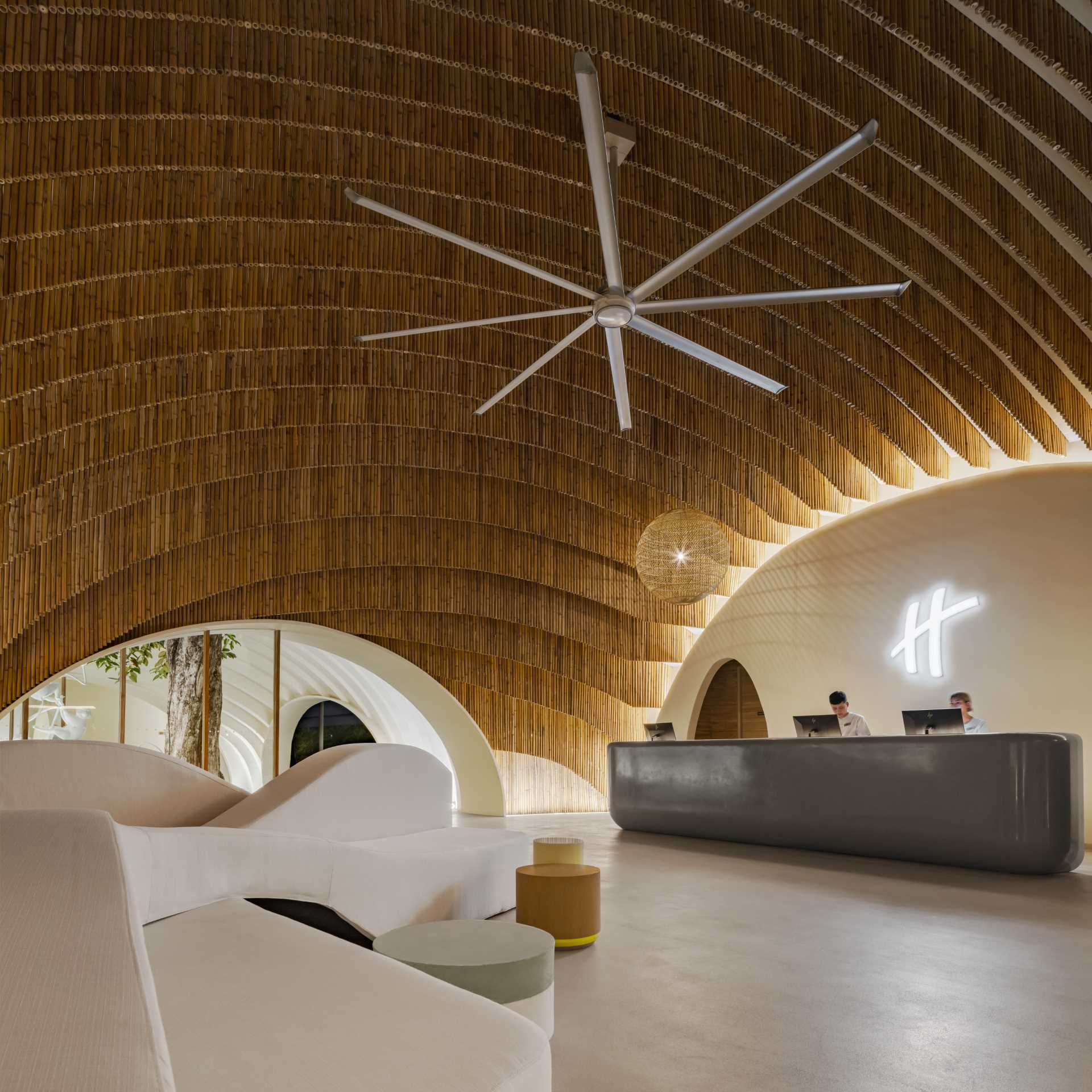 A modern hotel lobby that includes curved walls, hanging planes of bamboo, and hidden lighting that highlights the design.