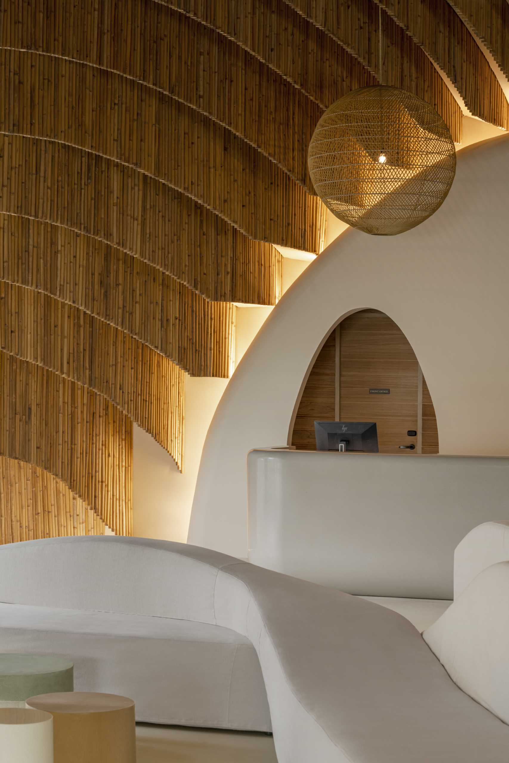 A modern hotel lobby that includes curved walls, hanging planes of bamboo, and hidden lighting that highlights the design.
