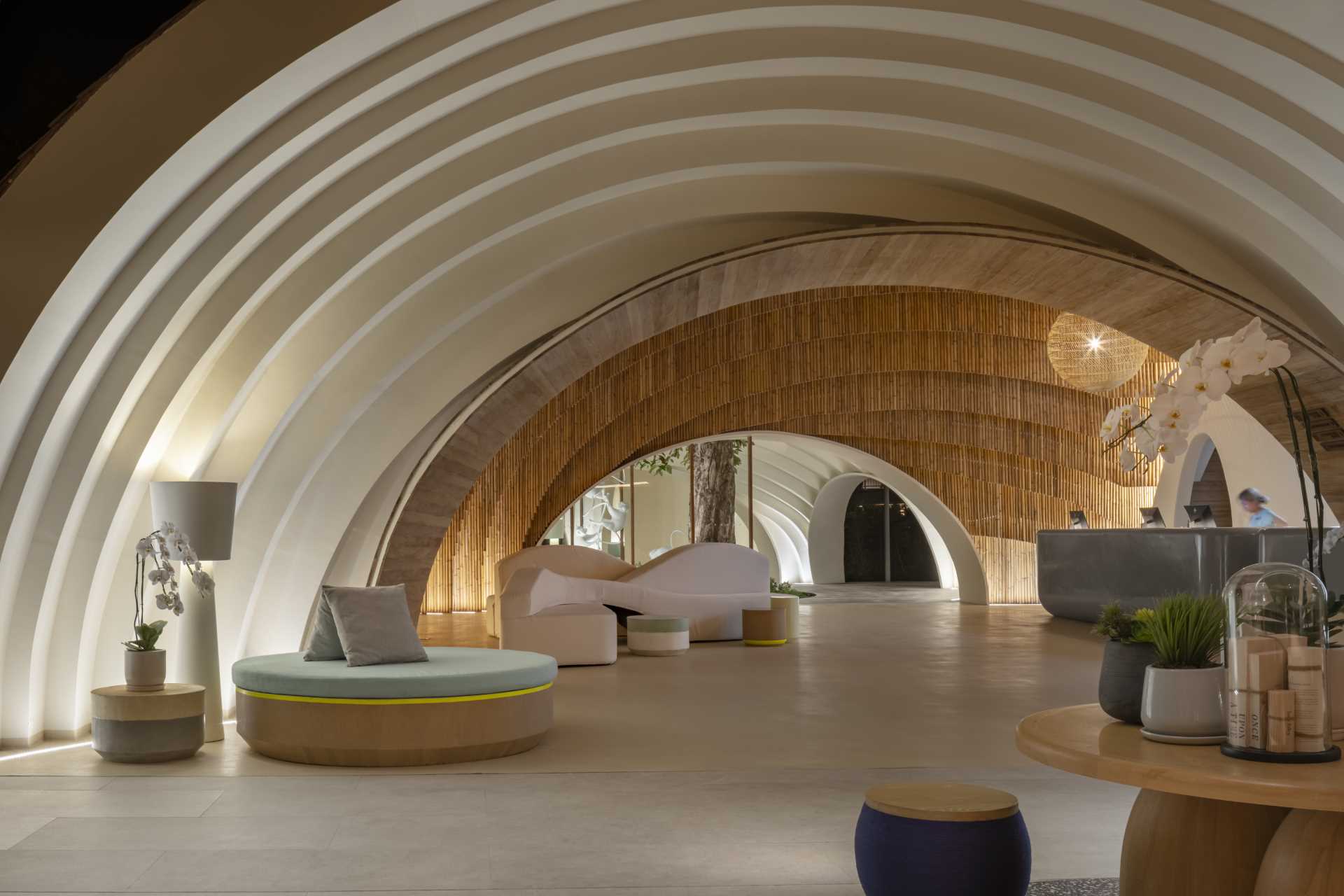 A modern hotel lobby that includes curved walls, hanging planes of bamboo, and hidden lighting that highlights the design.