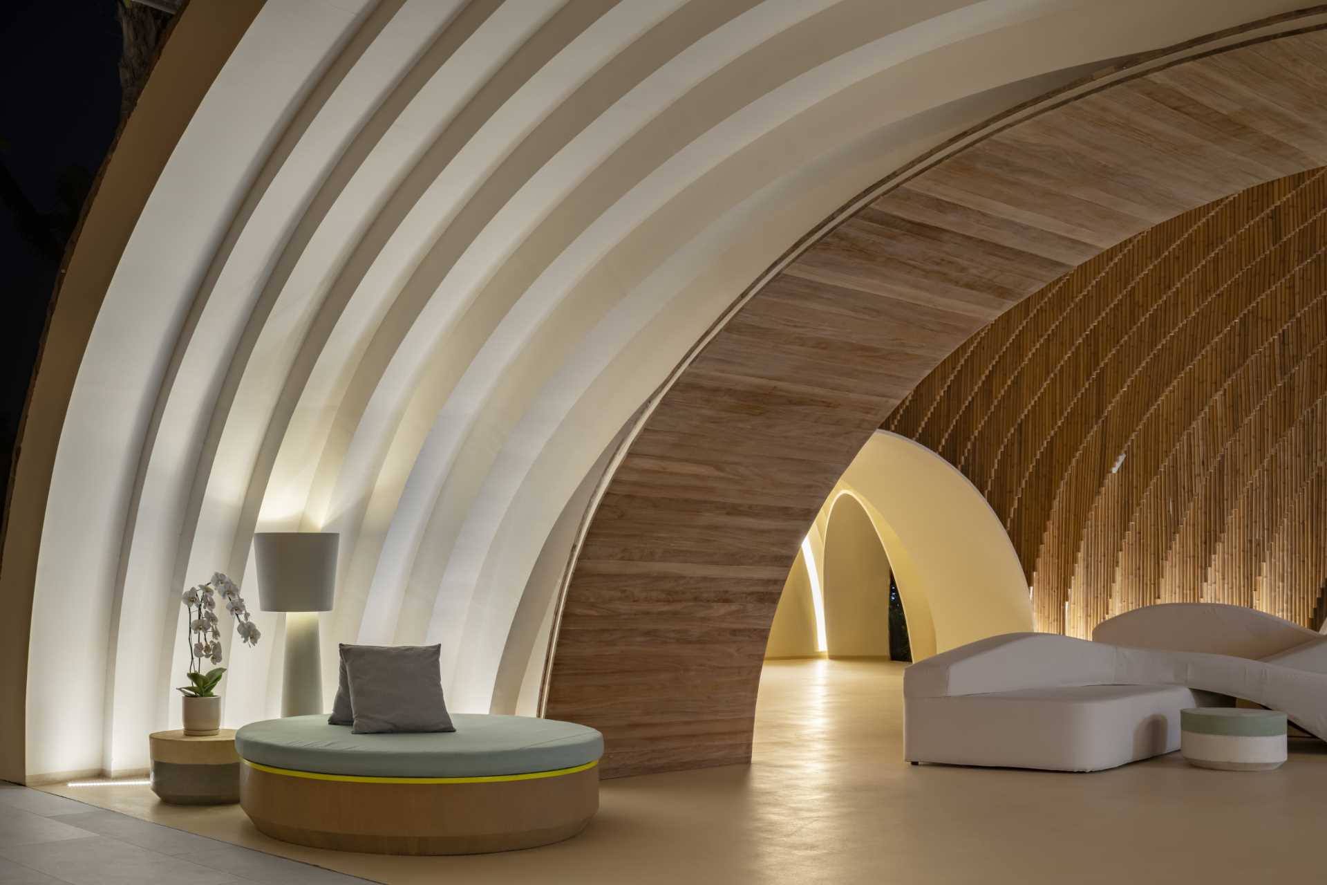 A modern hotel lobby that includes curved walls, hanging planes of bamboo, and hidden lighting that highlights the design.