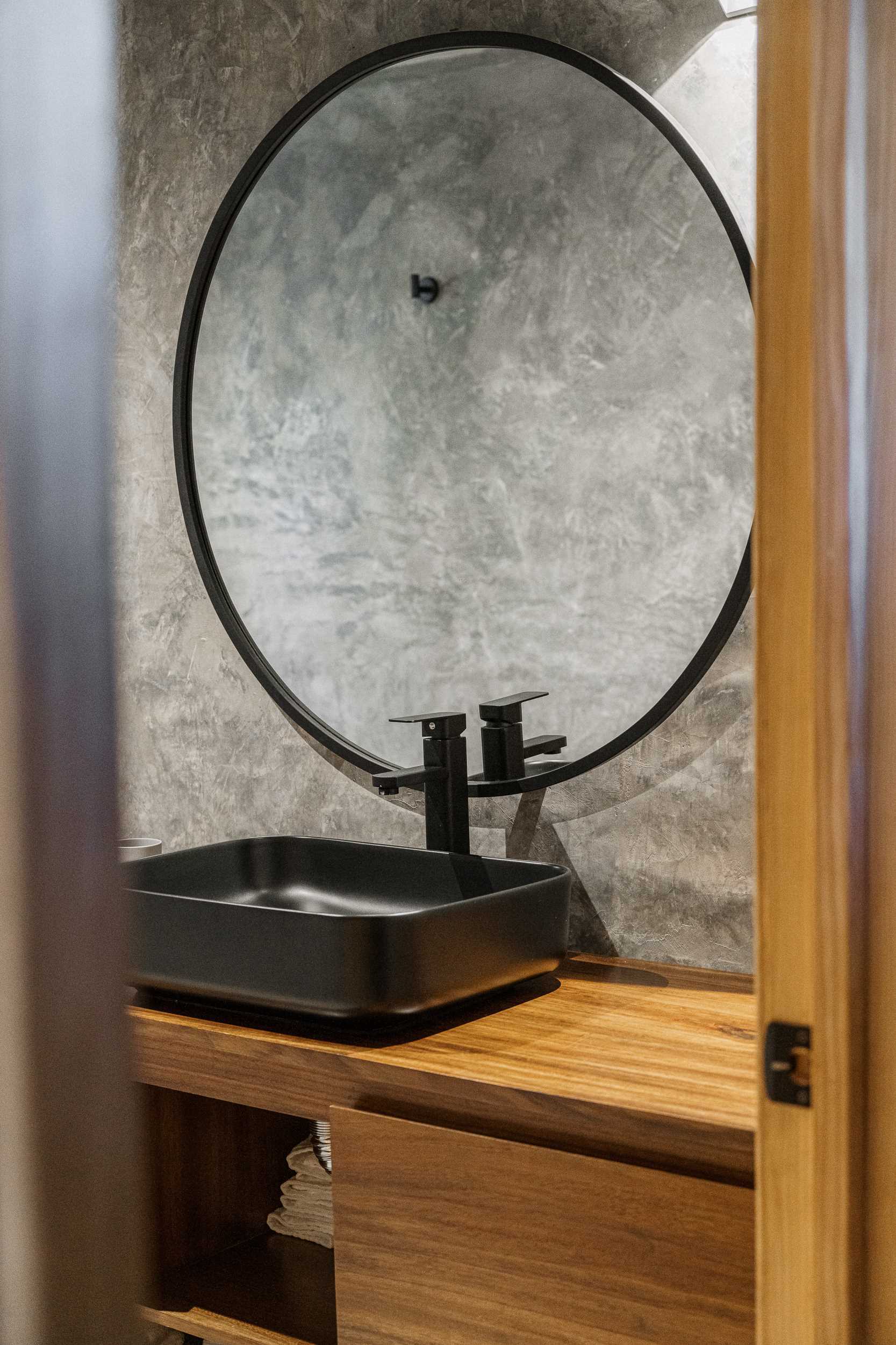 A modern stone and wood bathroom that includes a partial wall that separates the shower from the rest of the space.