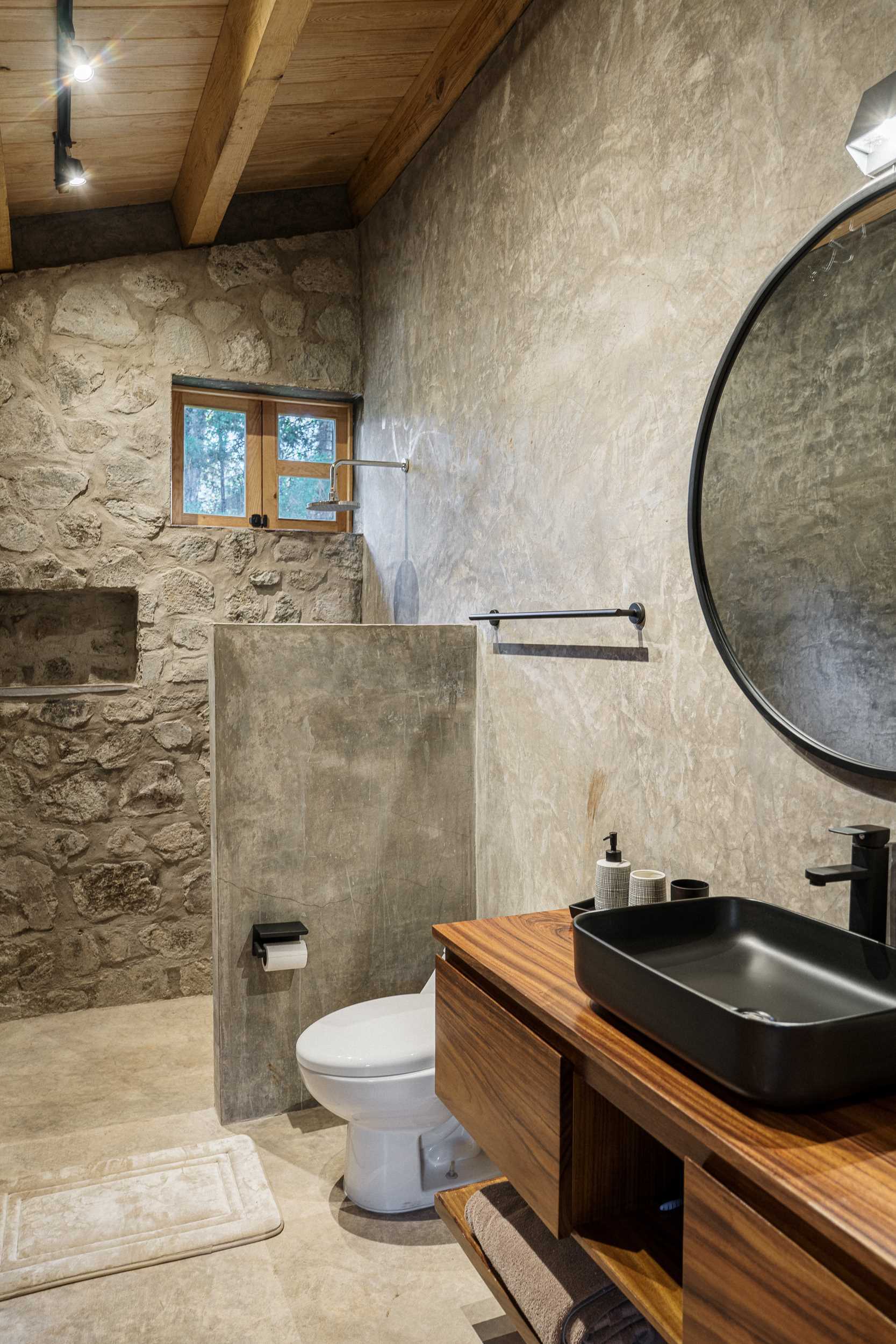 A modern stone and wood bathroom that includes a partial wall that separates the shower from the rest of the space.